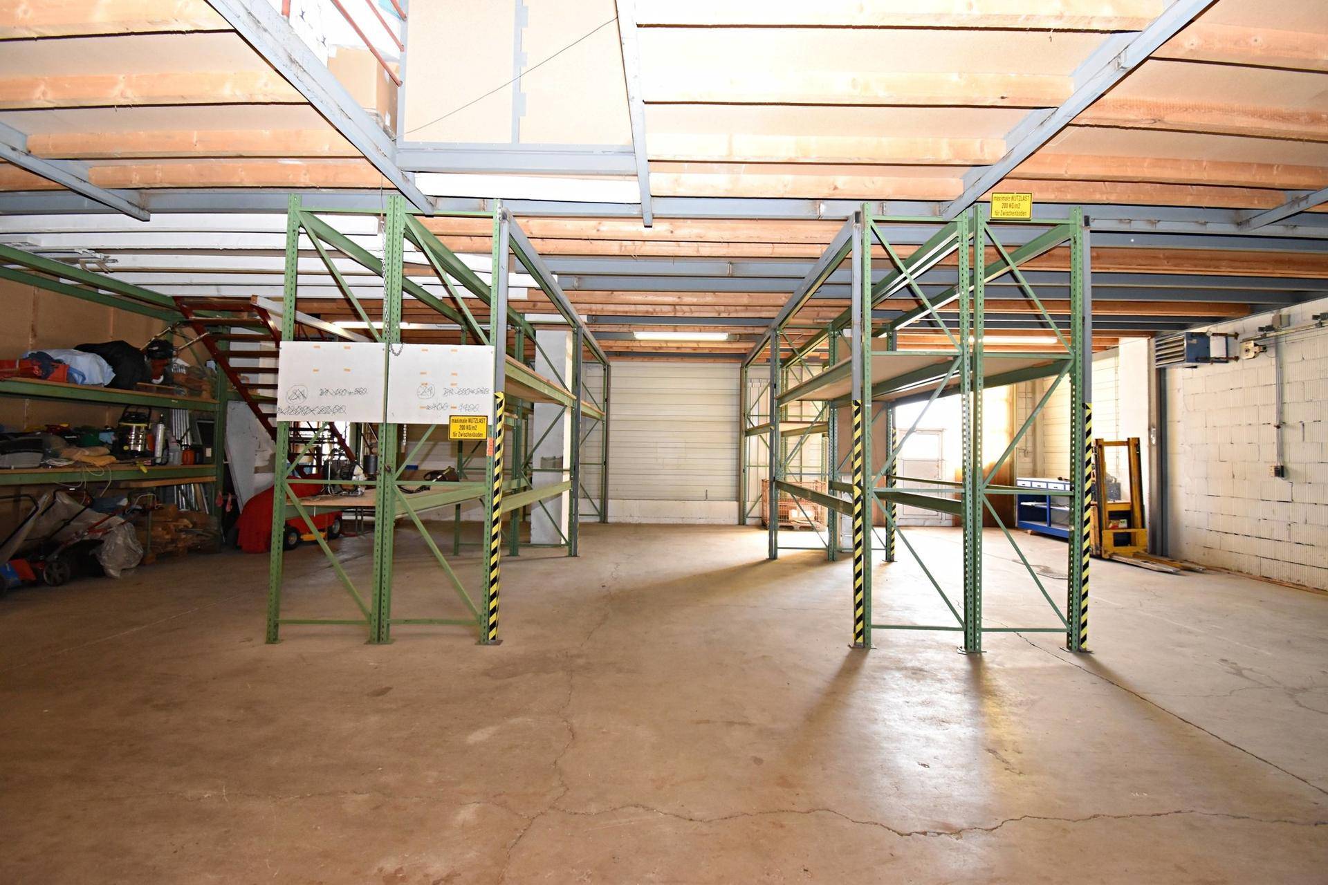 Geräumige Lagerhalle mit hohen Regalen, Betonboden und Rolltor im Hintergrund.