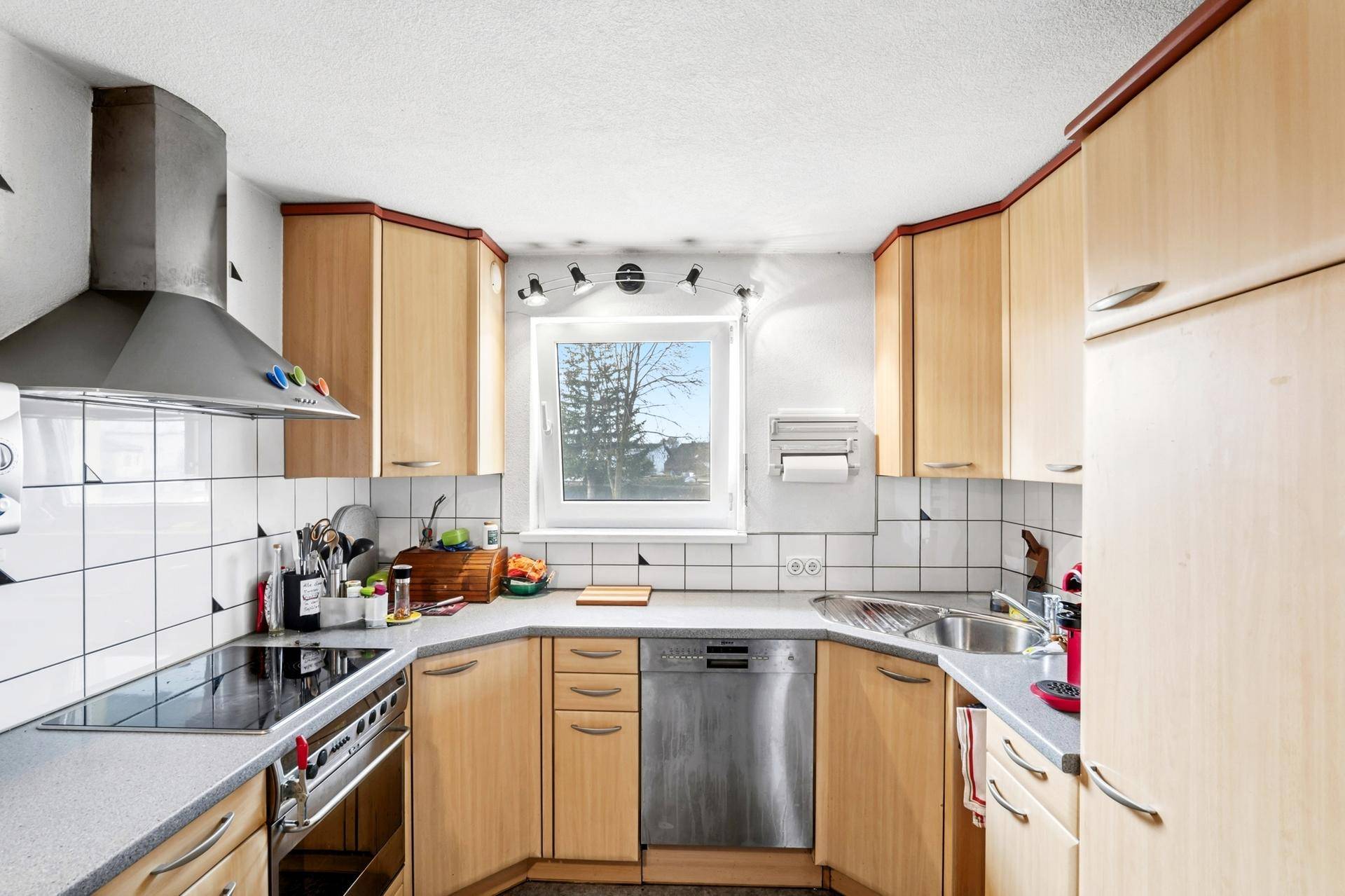 Helle Küche mit Holzfronten, Induktionskochfeld, Spülmaschine und Fenster.