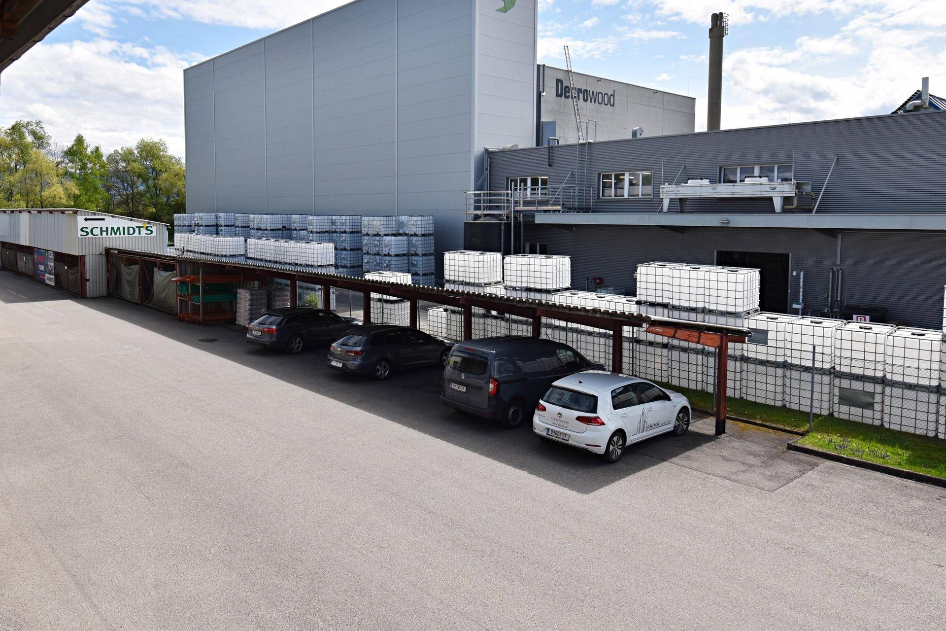 Überdachter Parkplatzbereich mit mehreren Fahrzeugen vor einem großen Industriegebäude.