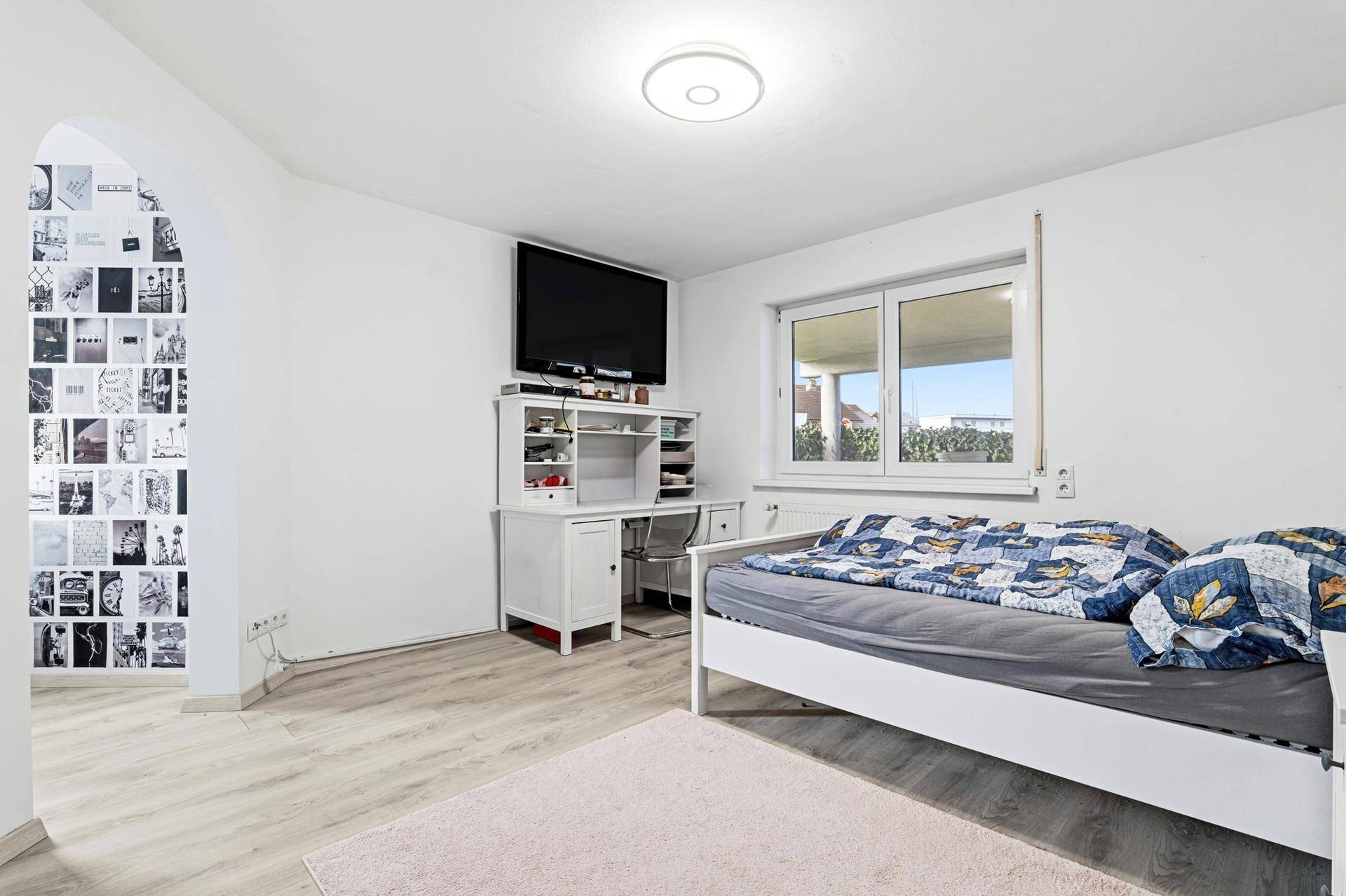 Schlafzimmer mit Laminatboden, Schreibtisch und Fernseher.