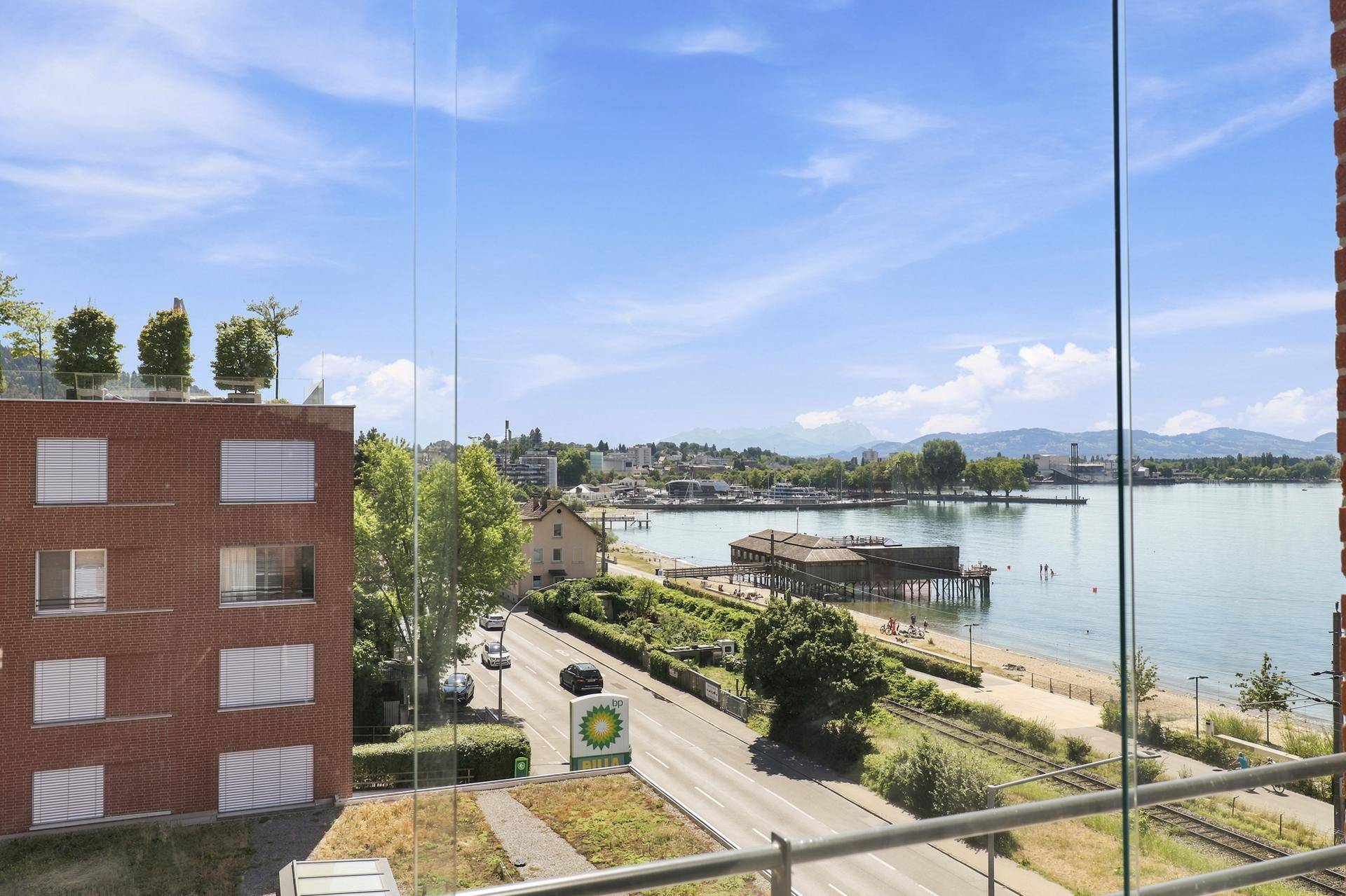 Ausblick auf den See, die Uferpromenade und die städtische Umgebung mit weiteren Gebäuden.
