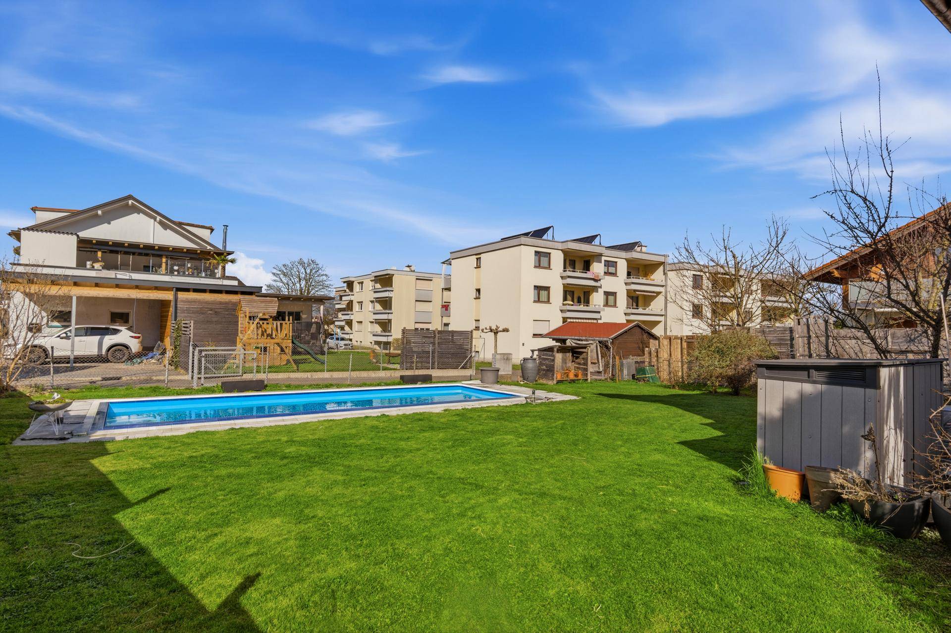 Großer Garten mit Rasenfläche, Swimmingpool und Spielplatz.