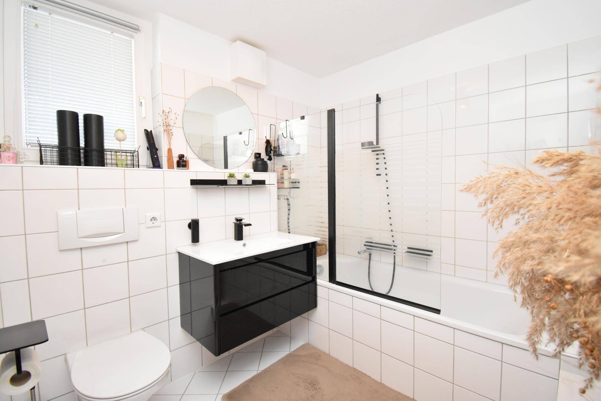 Modernes Badezimmer mit weißen Fliesen, Badewanne mit Duschabtrennung und schwarzem Waschtisch.