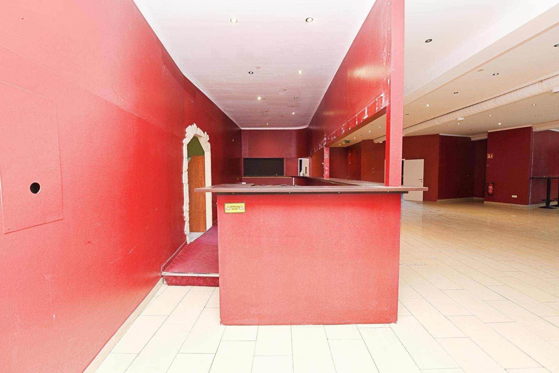 Innenansicht eines Barbereichs mit roter Wandfarbe und Theke, bereit zur Renovierung oder Neugestaltung.