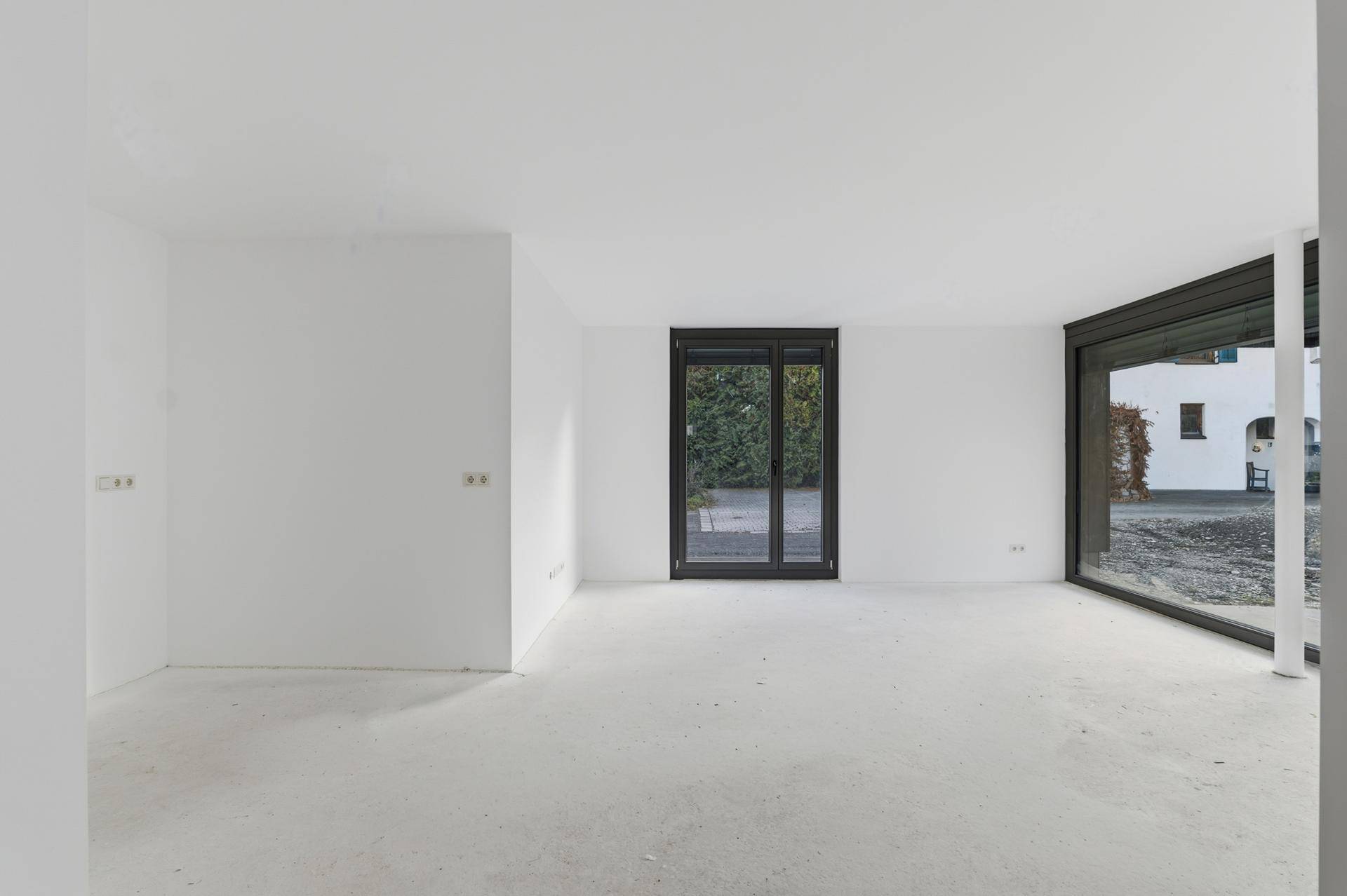 Heller, leerer Raum mit großen Fenstern und Zugang zum Außenbereich, bereit für den Ausbau.