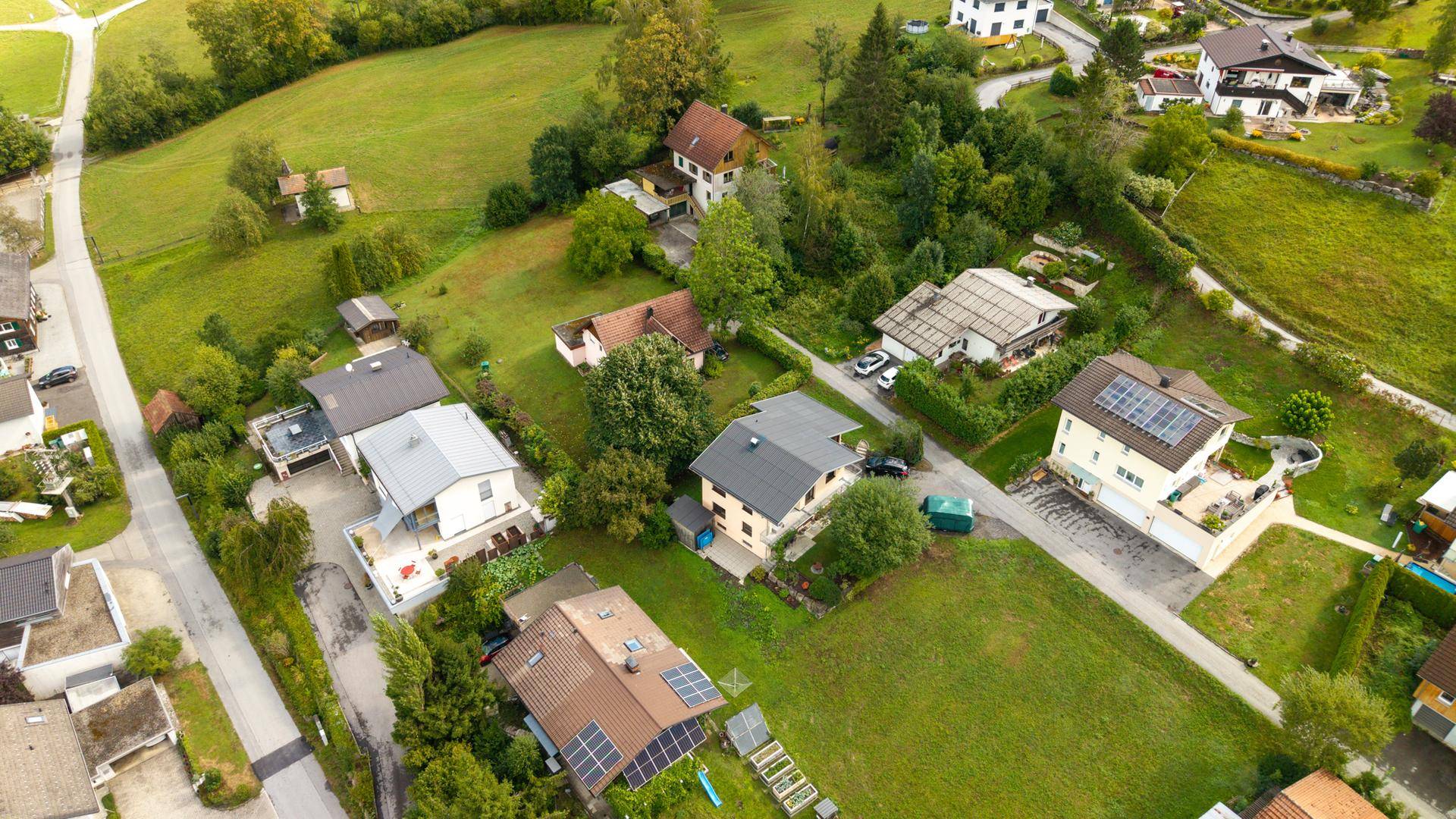 Weitläufige Luftaufnahme einer ländlichen Wohnsiedlung eingebettet in grüne Hügel und Wälder.