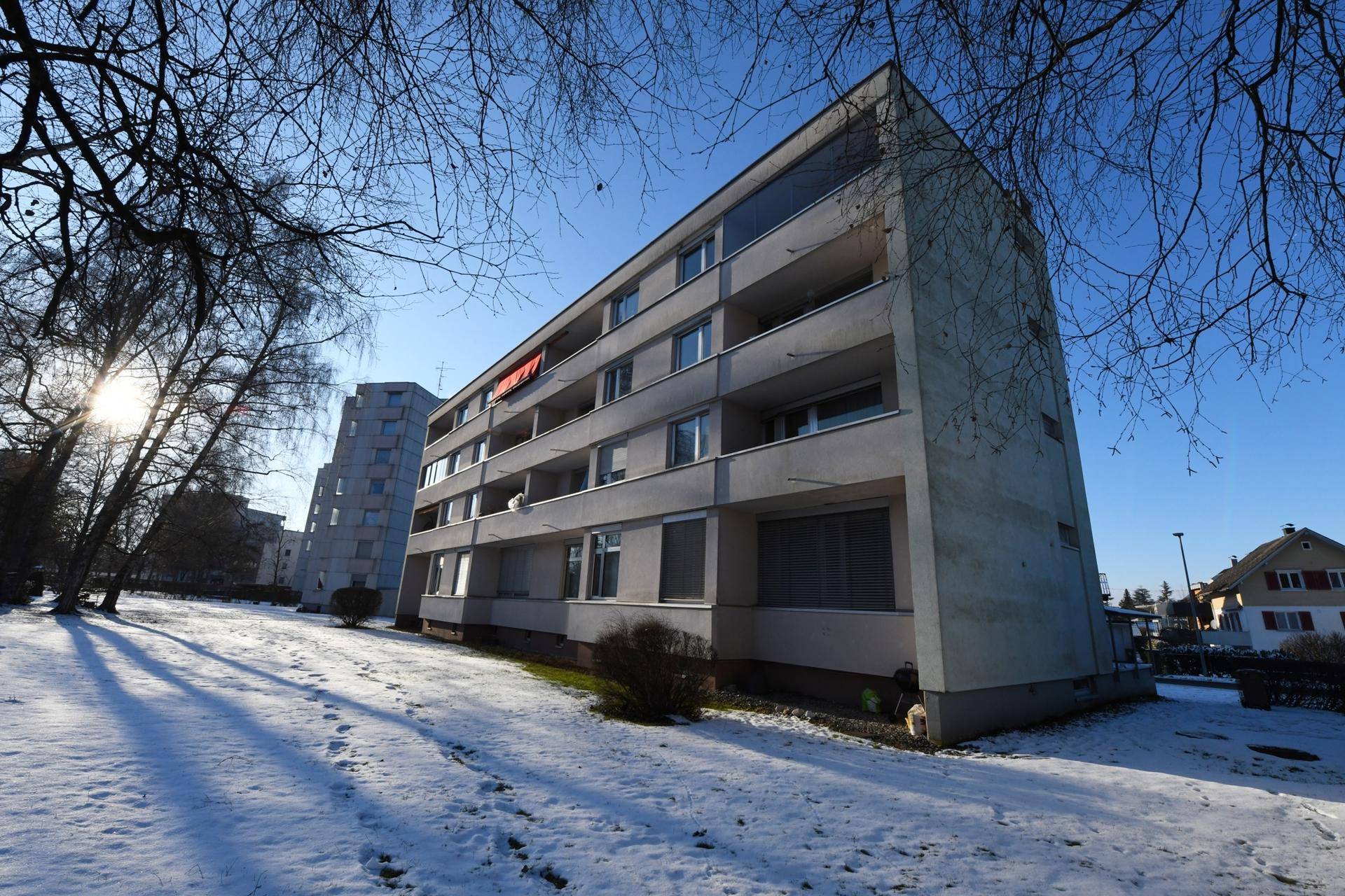 Mehrfamilienhaus in winterlicher Umgebung mit Schnee und Bäumen.