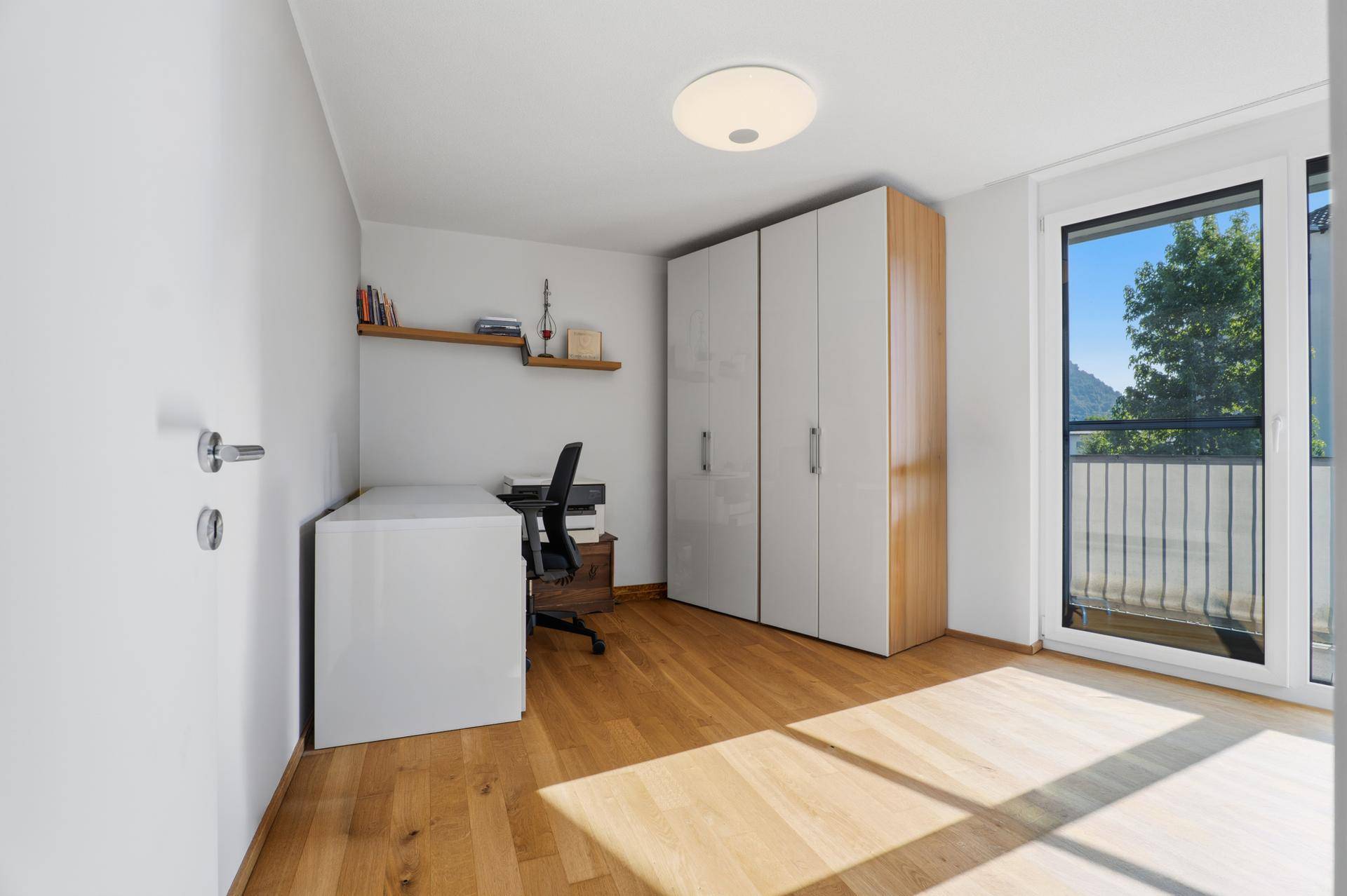 Helles Arbeitszimmer mit Holzboden, Schrank und Zugang zum Balkon.