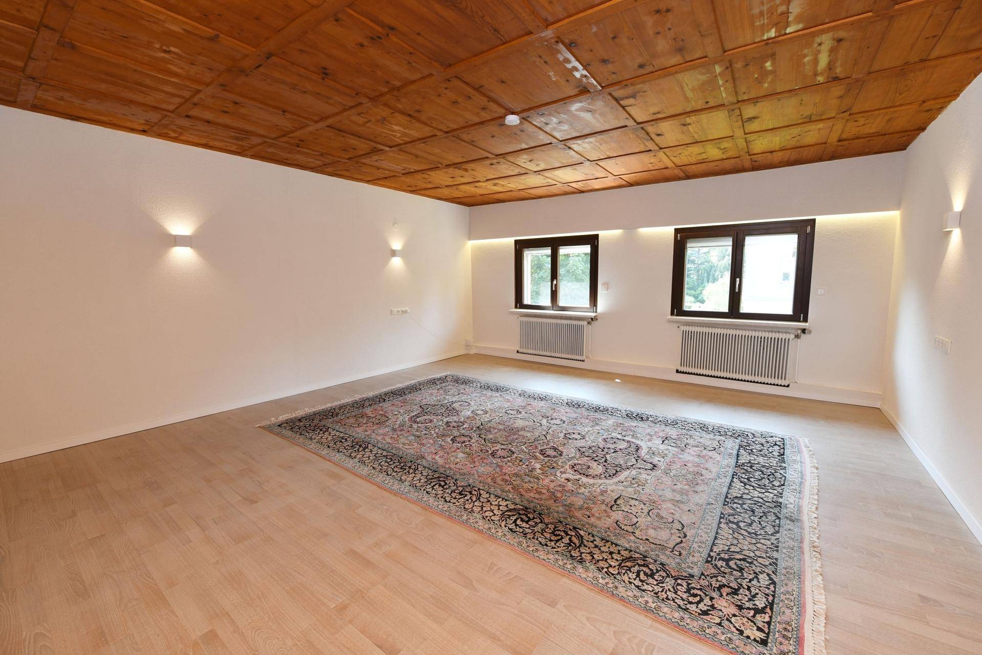 Geräumiges Zimmer mit charakteristischer Holzkassettendecke, Parkettboden und Wandbeleuchtung.