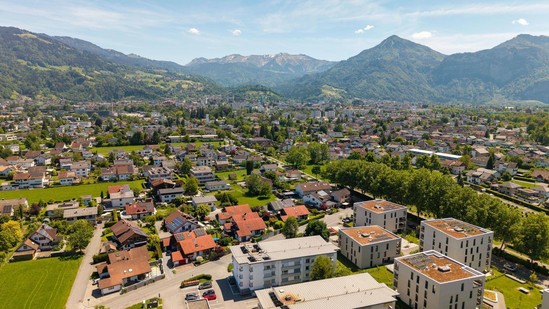 Weitwinkel-Luftaufnahme einer Stadtlandschaft mit Bergen und grünen Flächen.