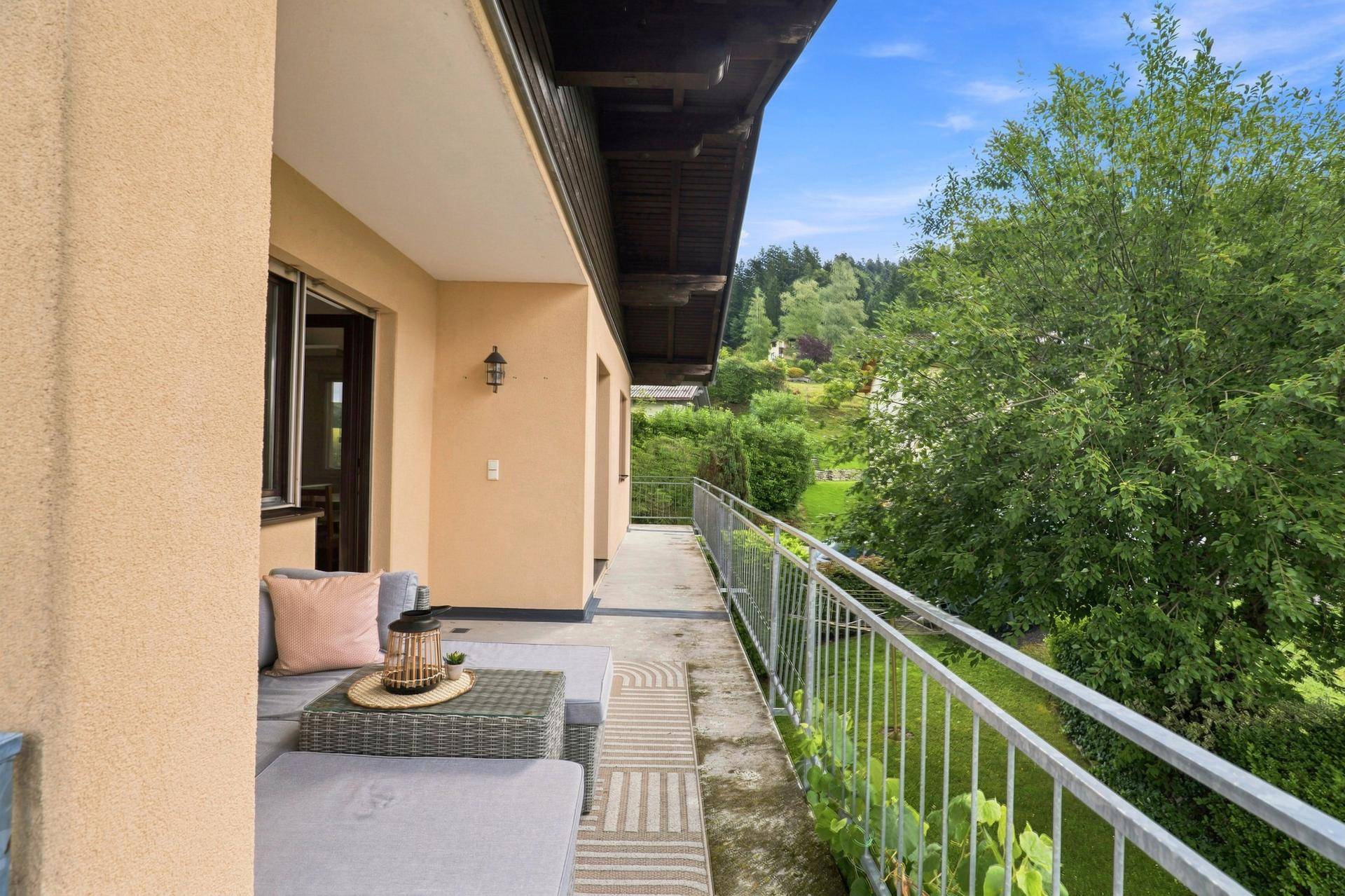 Langer Balkon mit moderner Sitzecke und Blick auf die umliegende grüne Natur und Bäume.