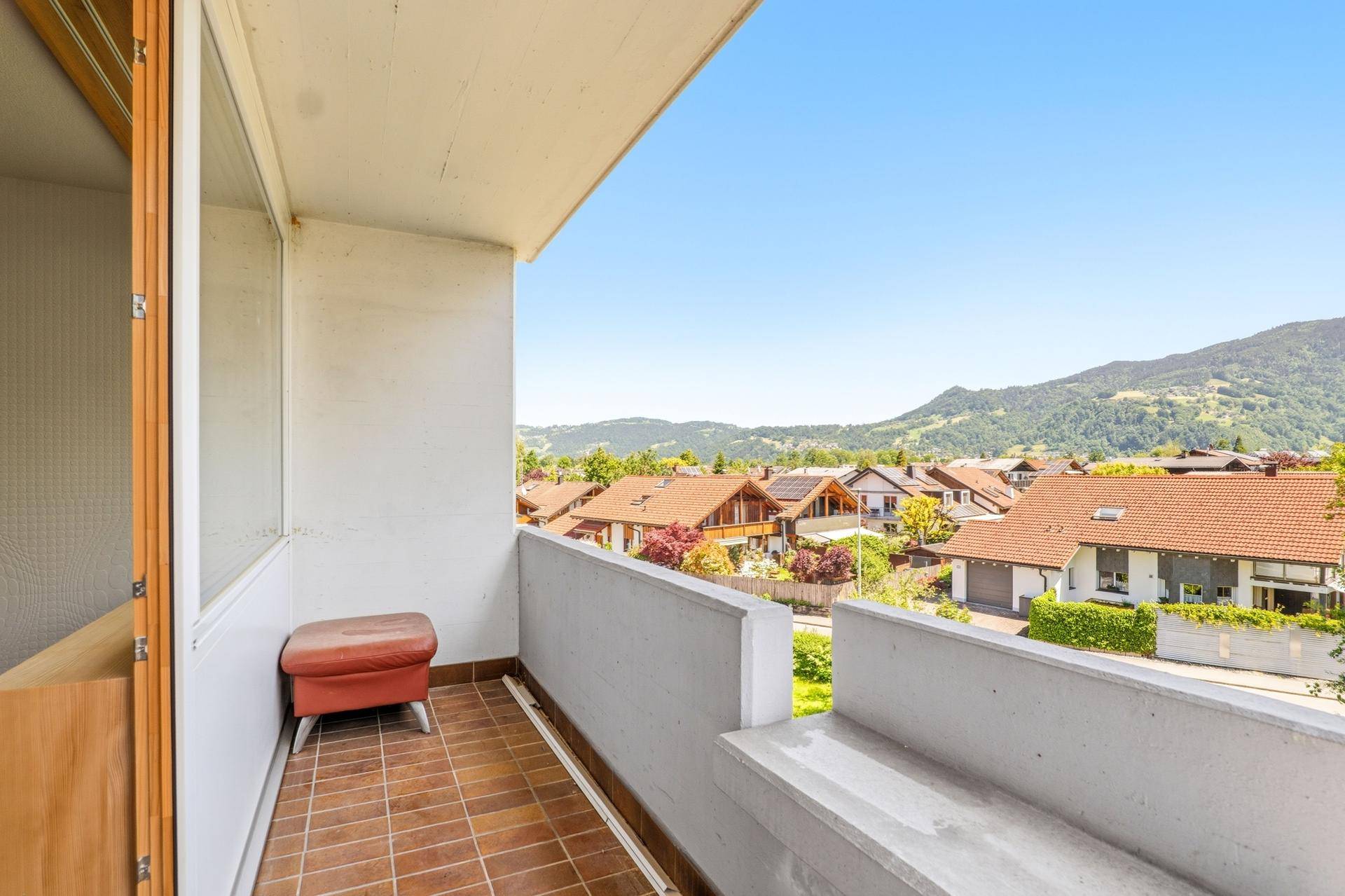 Balkon mit Fliesenboden und weitem Blick über Dächer und grüne Hügel.