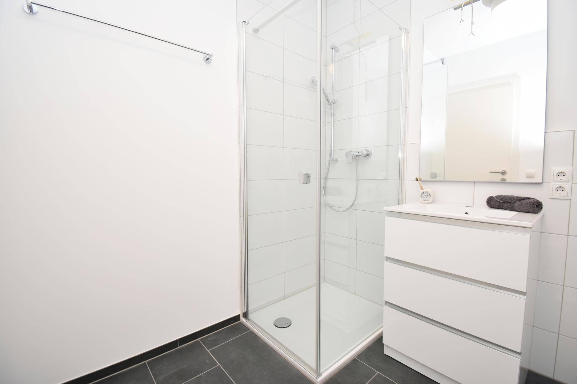 Helles Badezimmer mit großer Glasdusche, modernem Waschtisch und dunklem Fliesenboden.