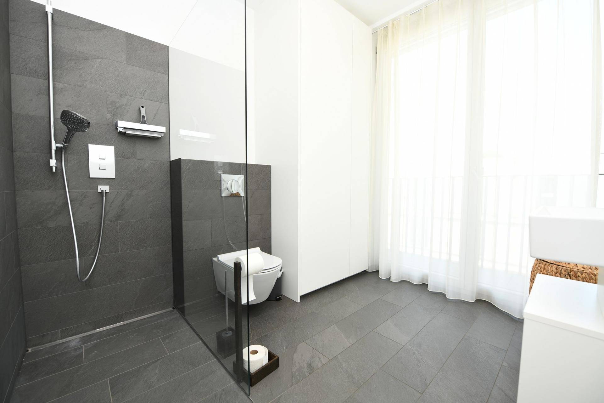 Modernes Badezimmer mit ebenerdiger Dusche, dunklen Fliesen und Fenster.
