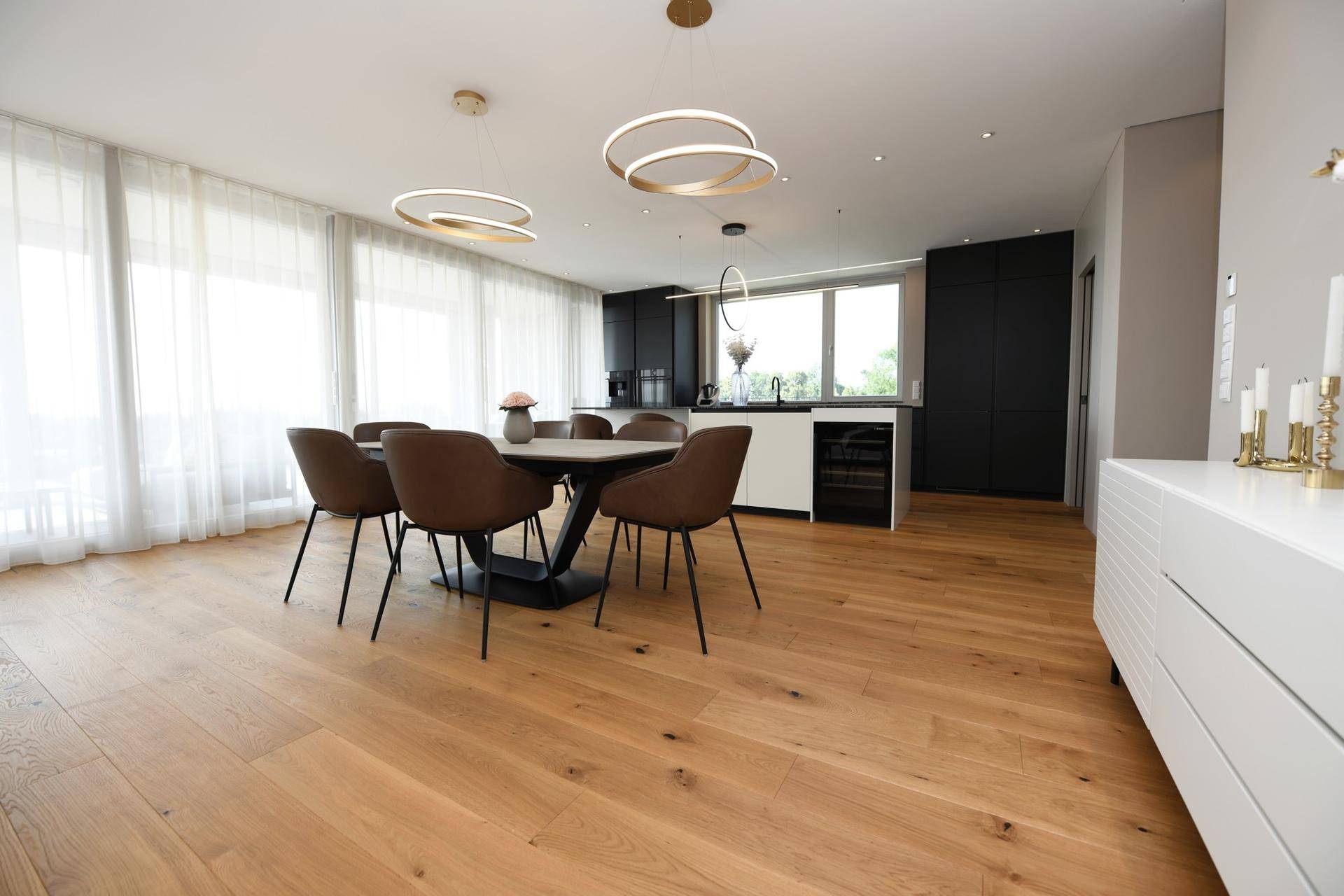 Heller Essbereich mit Holzboden, angrenzender moderner Küche und großen Fenstern.