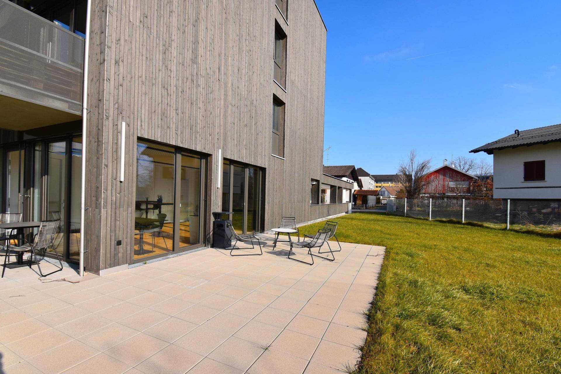 Große gepflasterte Terrasse mit Rasenfläche und Blick auf die Umgebung des Neubaus.
