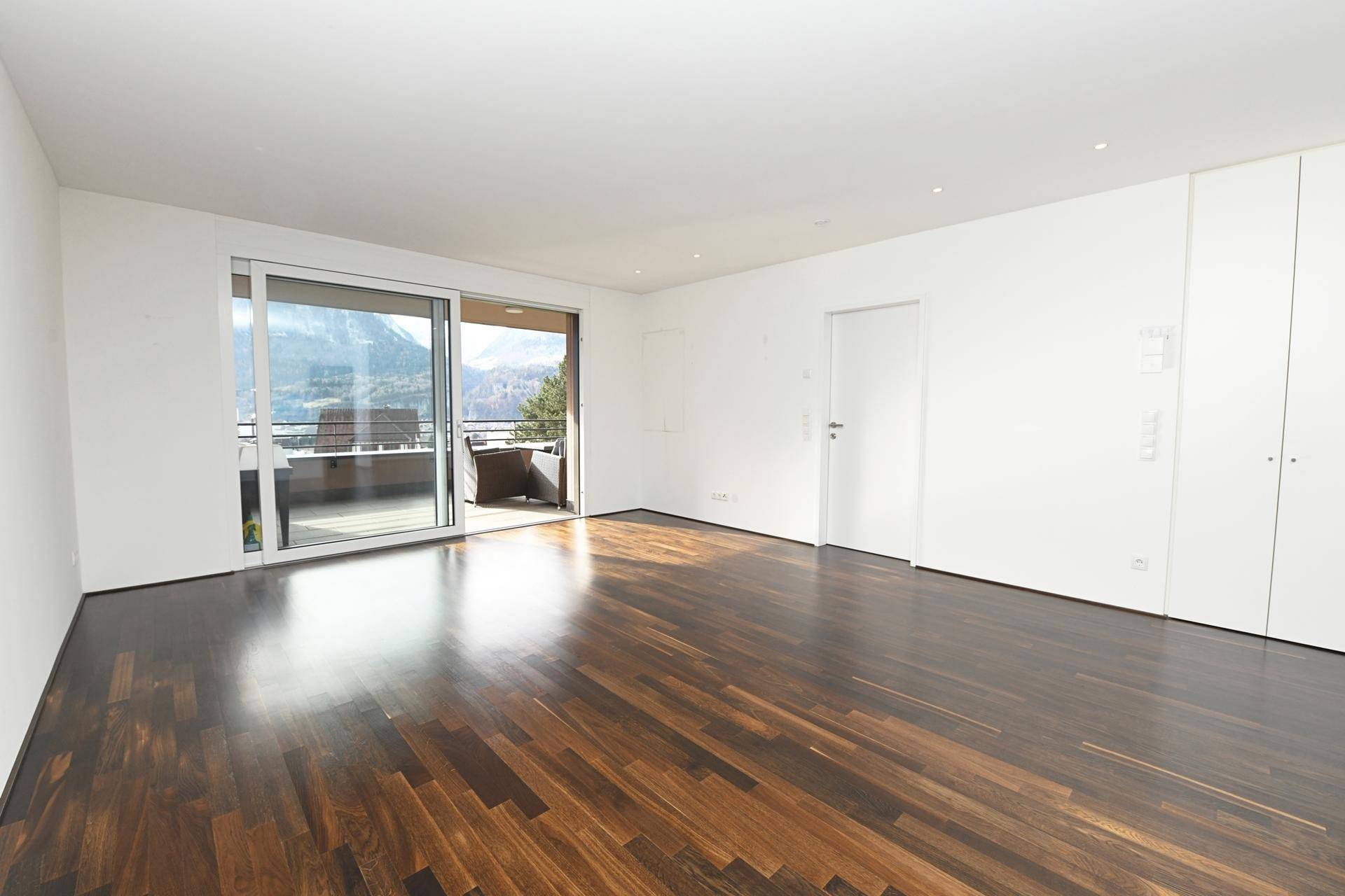 Leeres Wohnzimmer mit großen Schiebetüren und Zugang zu einem Balkon mit Bergblick.