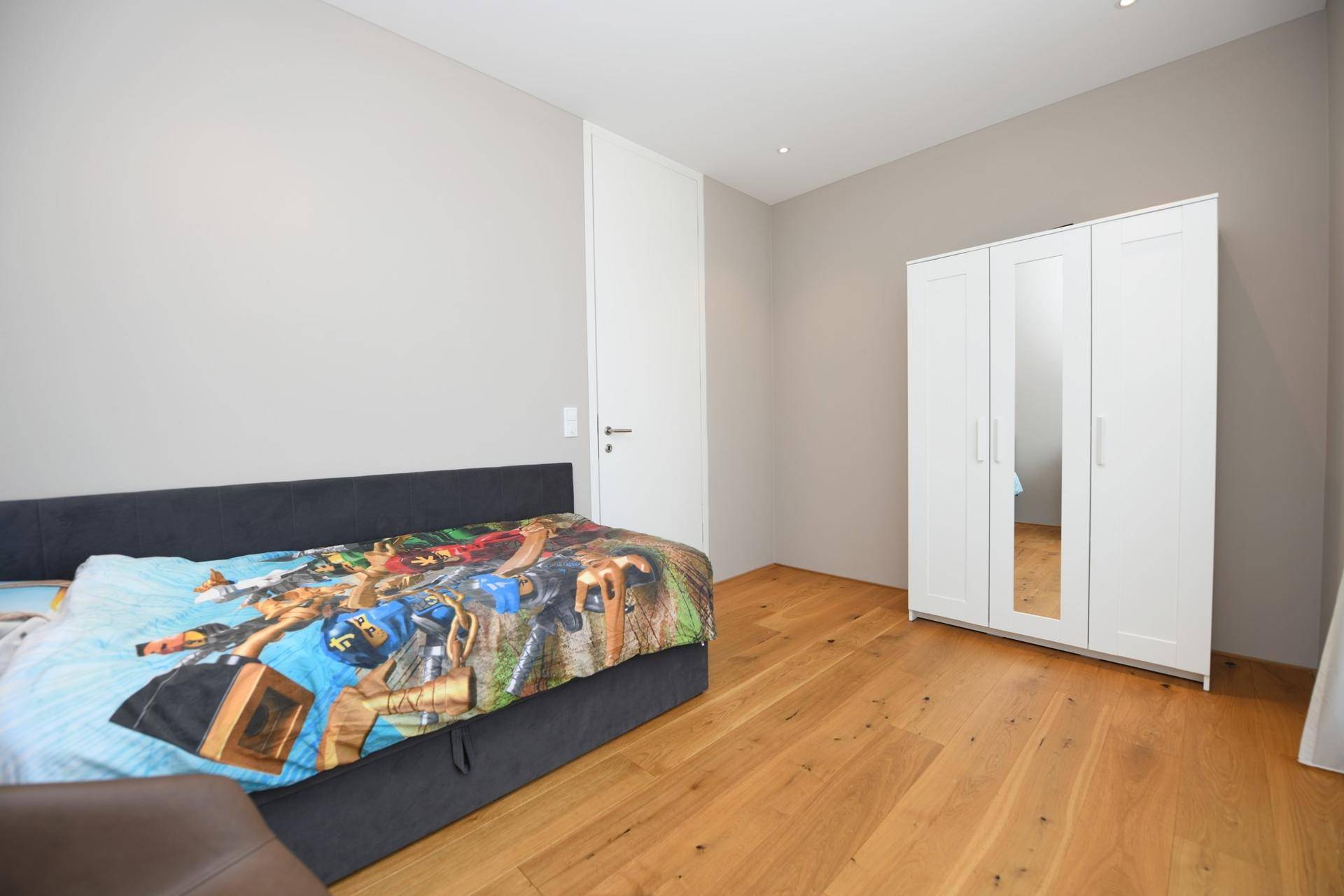 Schlafzimmer mit Holzboden, weißem Kleiderschrank und Einzelbett.