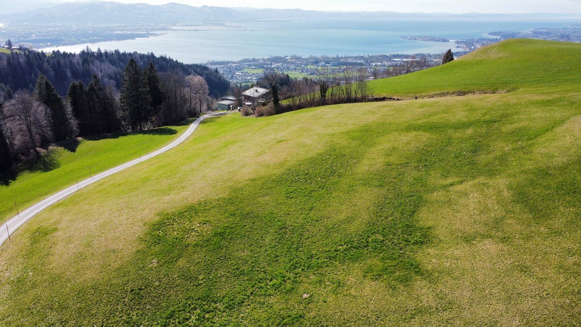 Panoramablick über grüne Hügel, einen See und die umliegende Landschaft mit Bergen im Hintergrund.