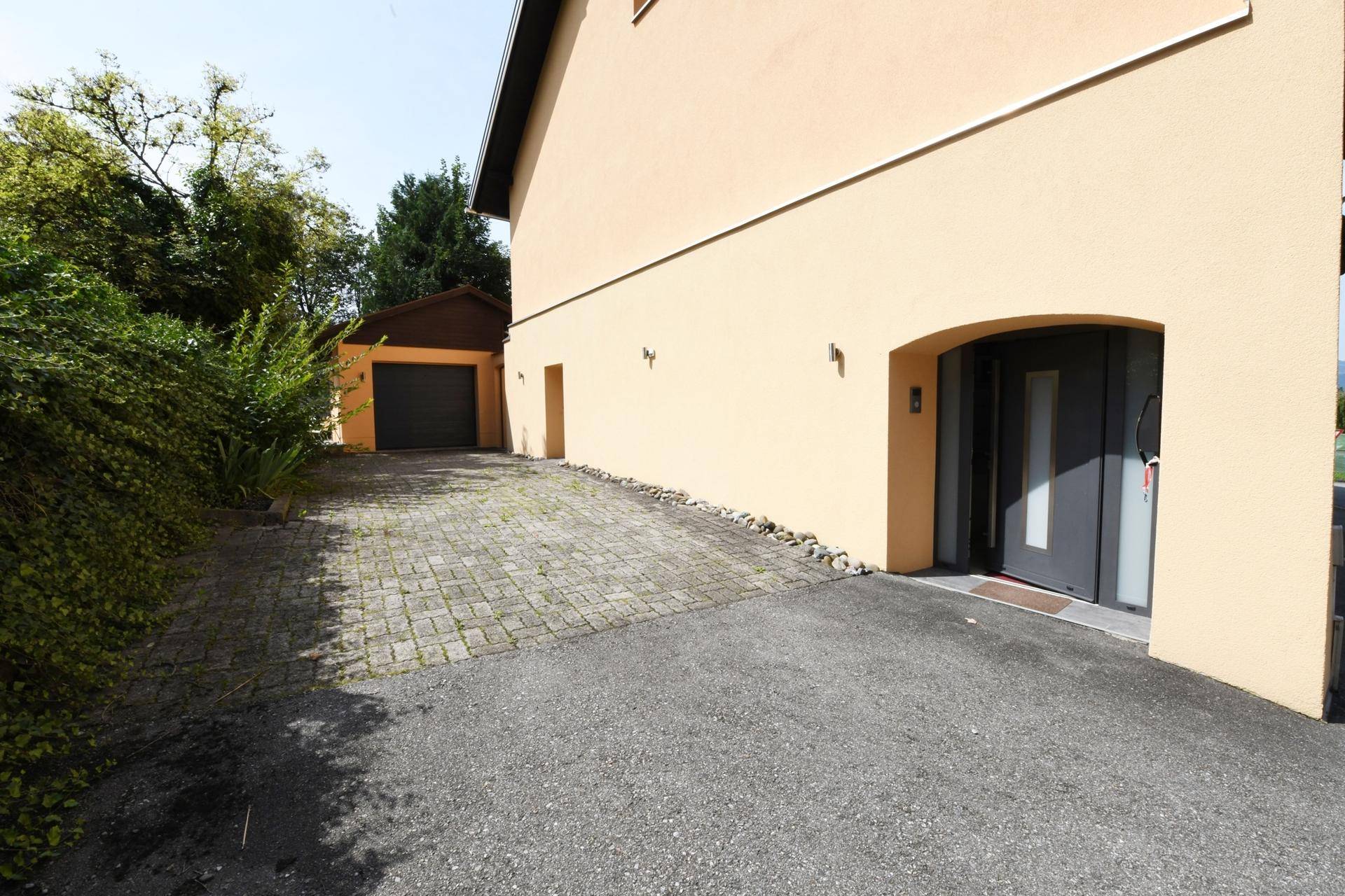 Hausfassade mit gepflasterter Einfahrt und separater Garage, gut gepflegt.