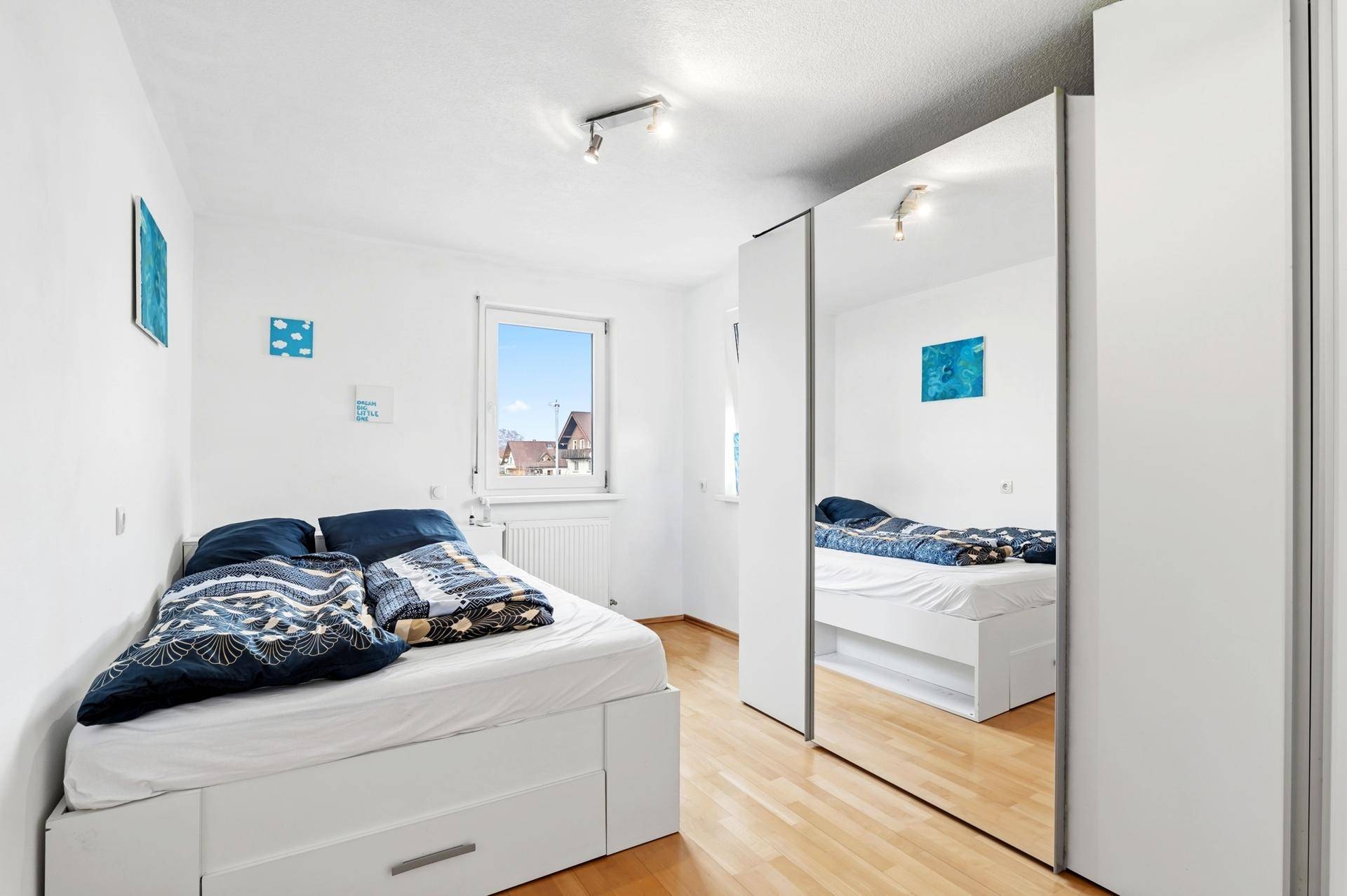 Schlafzimmer mit Holzboden, weißem Bett und großem Spiegelschrank.