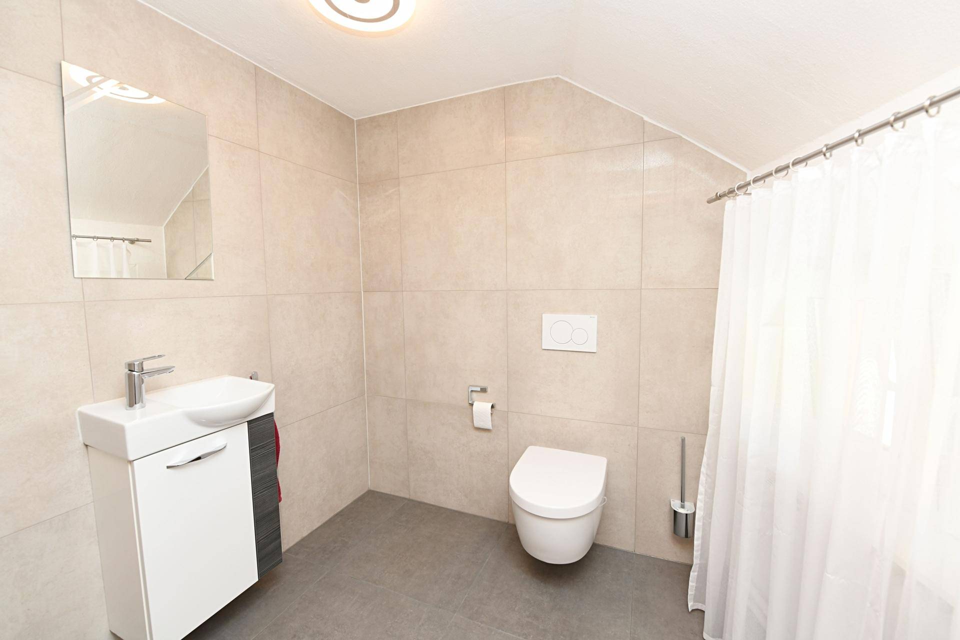 Gäste-WC mit wandhängendem WC, Waschbecken und Duschvorhang in heller Gestaltung.
