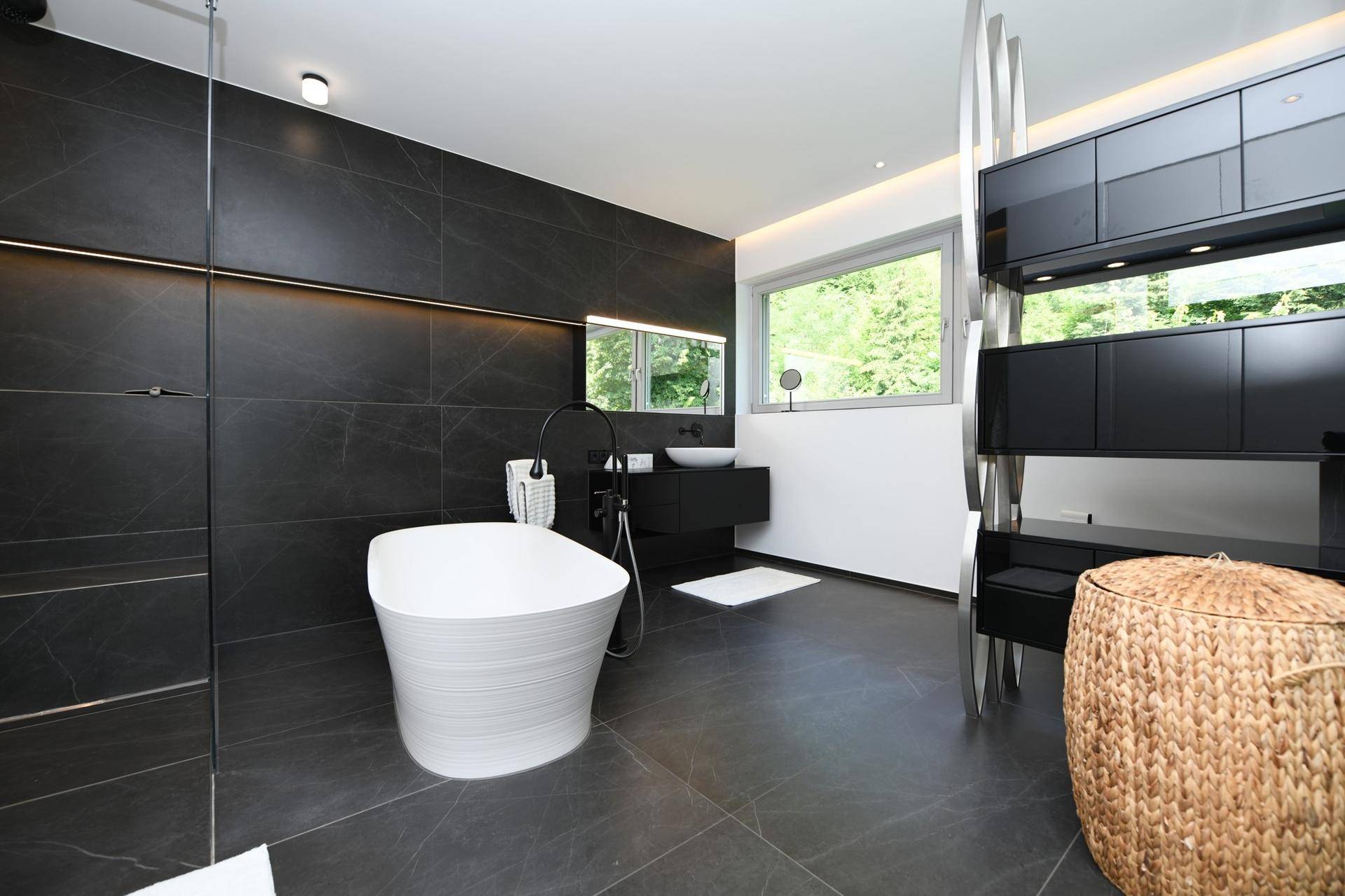 Modernes Badezimmer mit dunklen Fliesen, freistehender Badewanne und Blick ins Grüne.