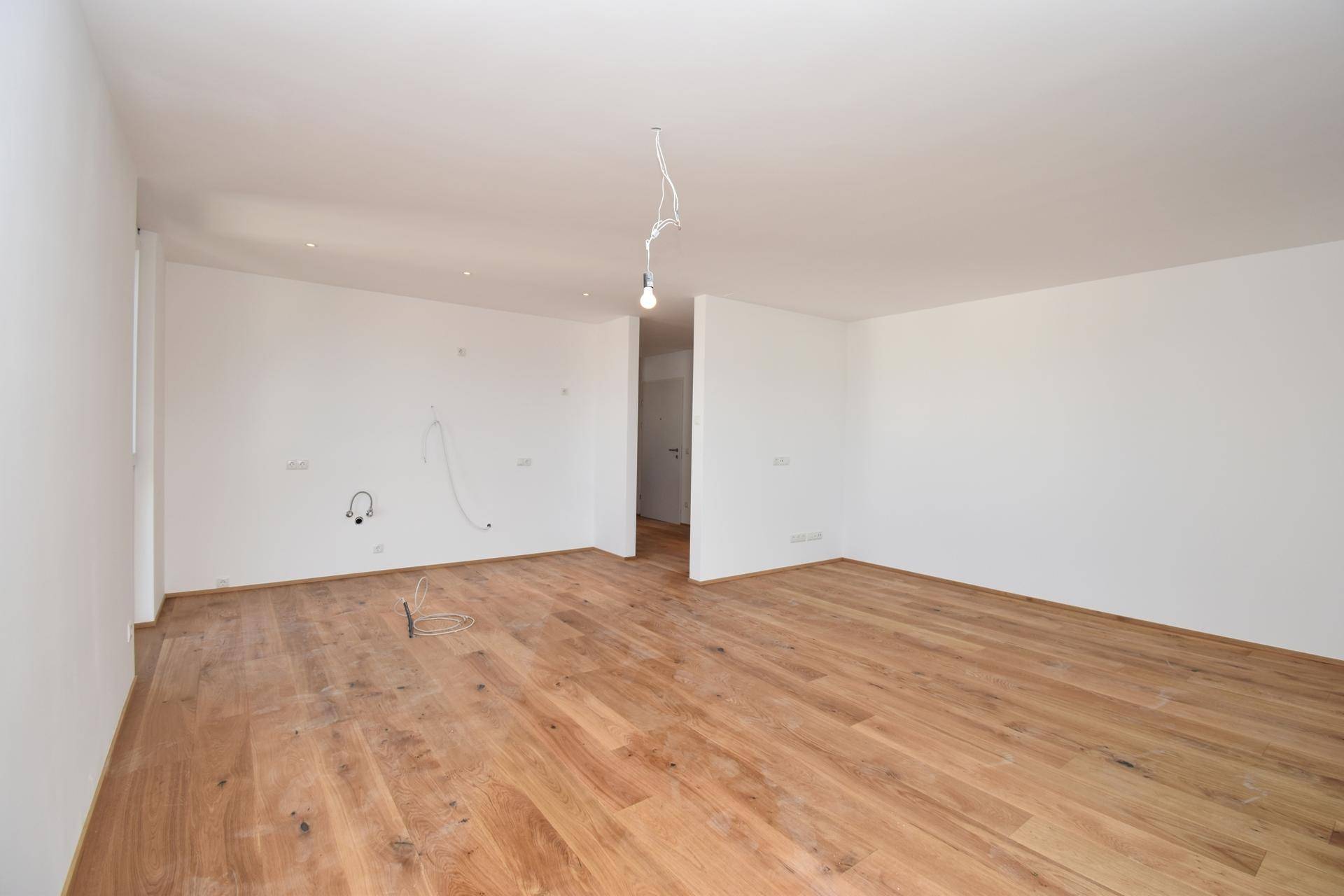 Heller, leerer Wohnraum mit neuem Holzparkettboden und weißen Wänden, bereit zum Einzug.