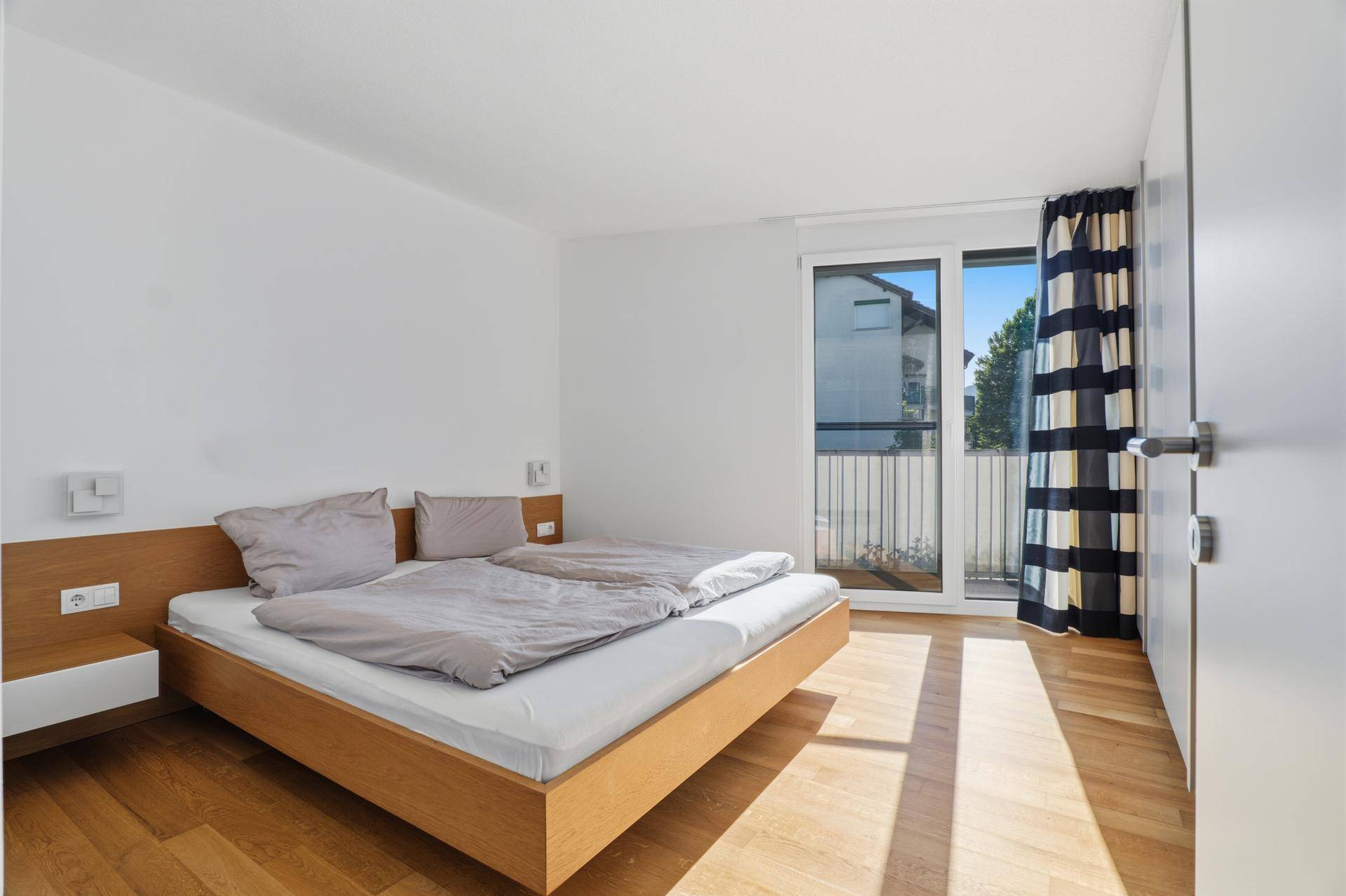 Helles Schlafzimmer mit Holzboden, modernem Bett und Zugang zum Balkon.