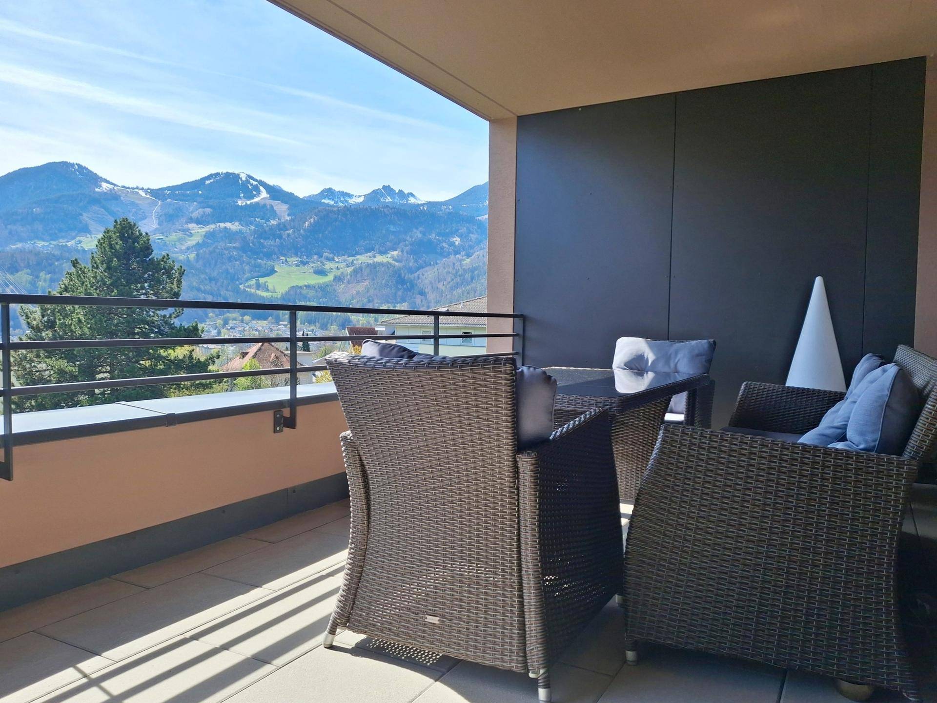 Balkon mit Sitzgelegenheiten und Blick auf grüne Hügel und Berge.