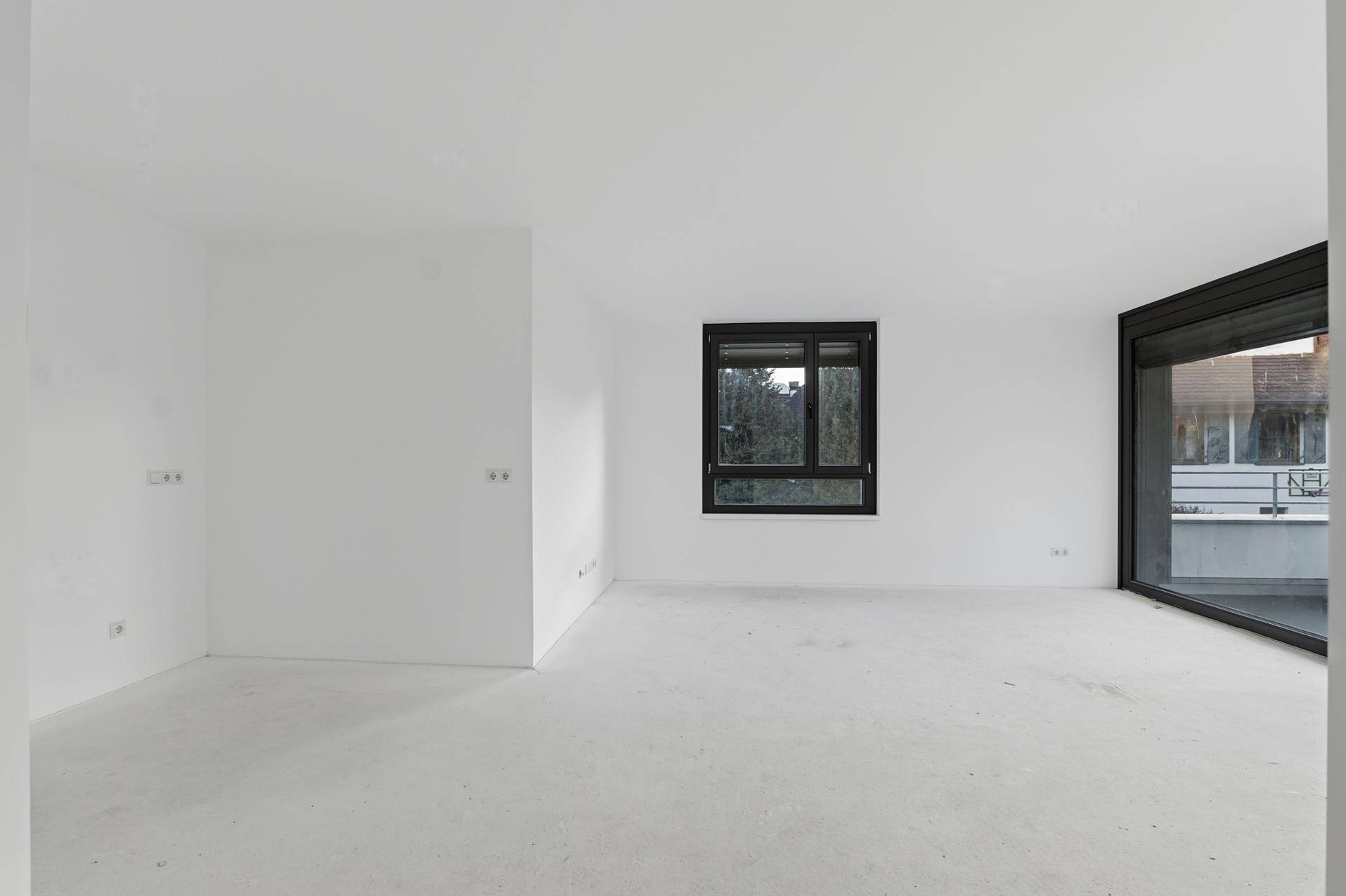 Leerer, heller Wohnraum mit großen Fenstern und Zugang zu einem Außenbereich, bereit für den Ausbau.