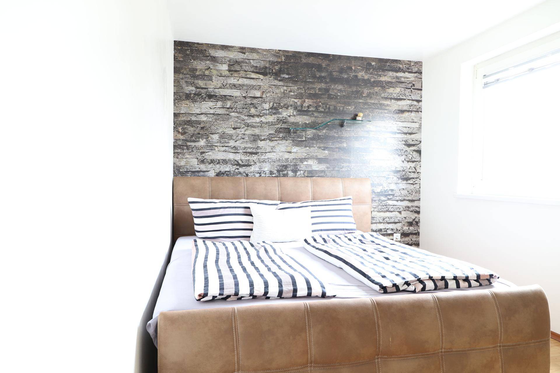 Helles Schlafzimmer mit Akzentwand in Steinoptik und bequemen Bett für erholsamen Schlaf.