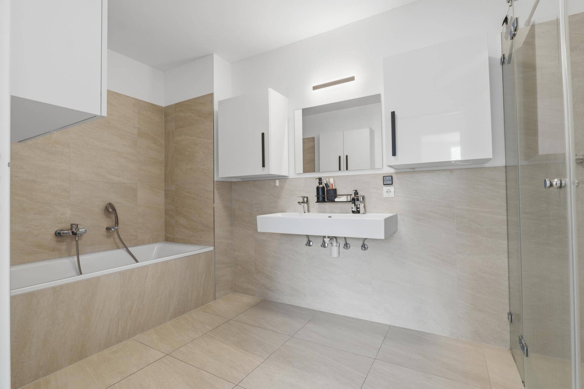 Modernes Badezimmer mit beigefarbenen Fliesen, Badewanne, schwebendem Waschbecken und Dusche.