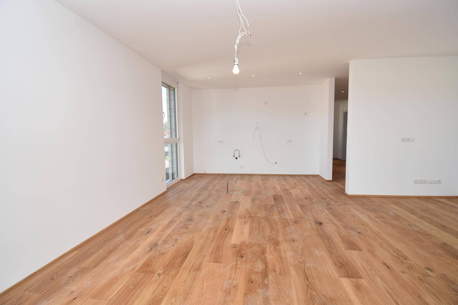Lichtdurchfluteter Wohnraum mit großen Fenstern und hochwertigem Holzparkettboden.