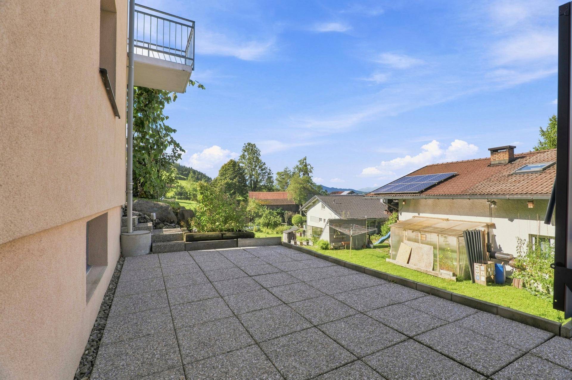 Große gepflasterte Terrasse mit weitem Blick auf die umliegende grüne Landschaft und Berge.