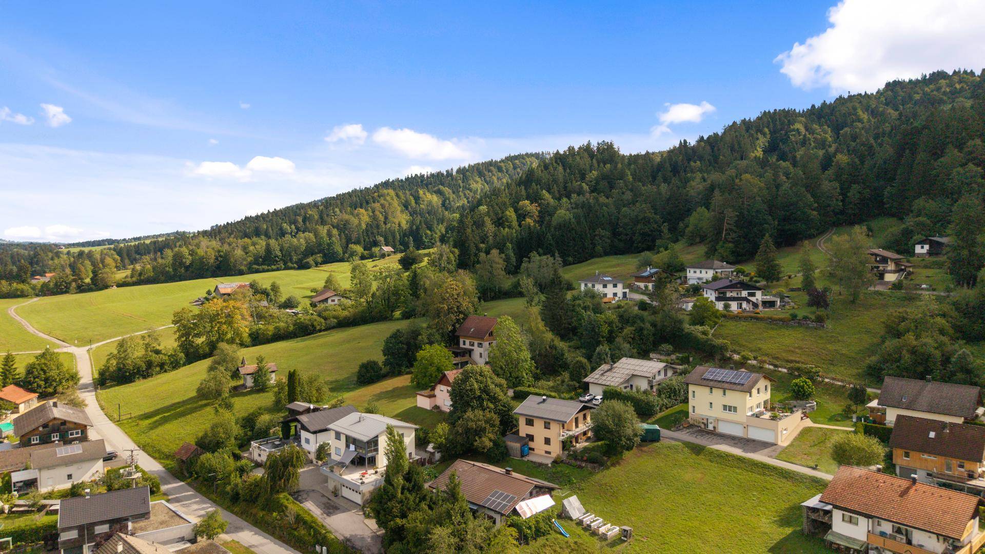 Weitläufige Luftaufnahme einer ländlichen Wohngegend mit Häusern, Feldern und bewaldeten Hügeln.