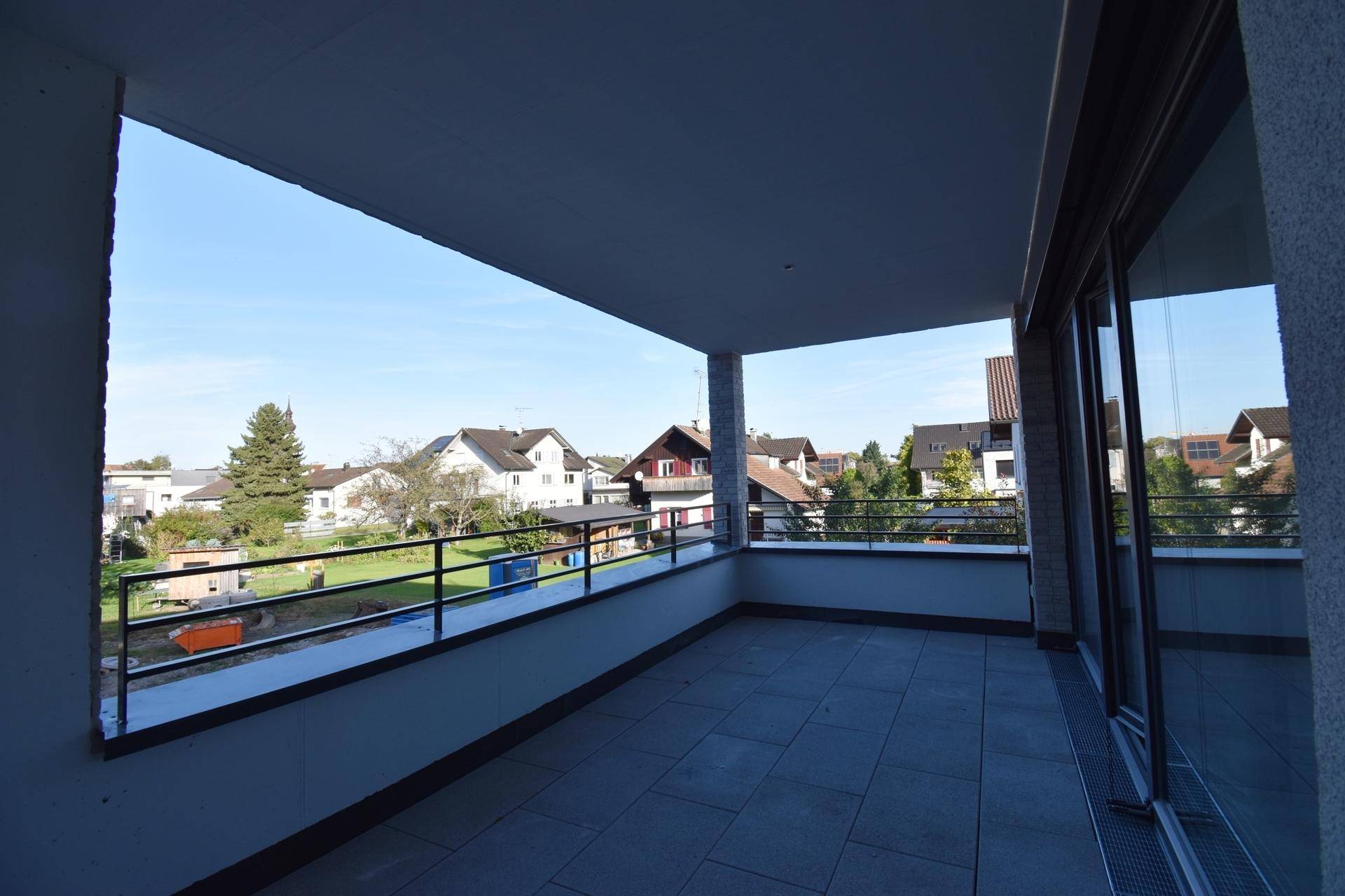 Großer, überdachter Balkon mit Fliesenboden und weitem Blick auf die grüne Umgebung.