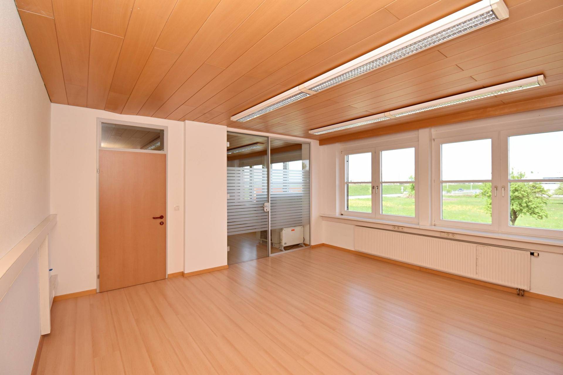 Heller Büroraum mit Laminatboden, Holzdecke und Glastrennwand zu einem weiteren Bereich.