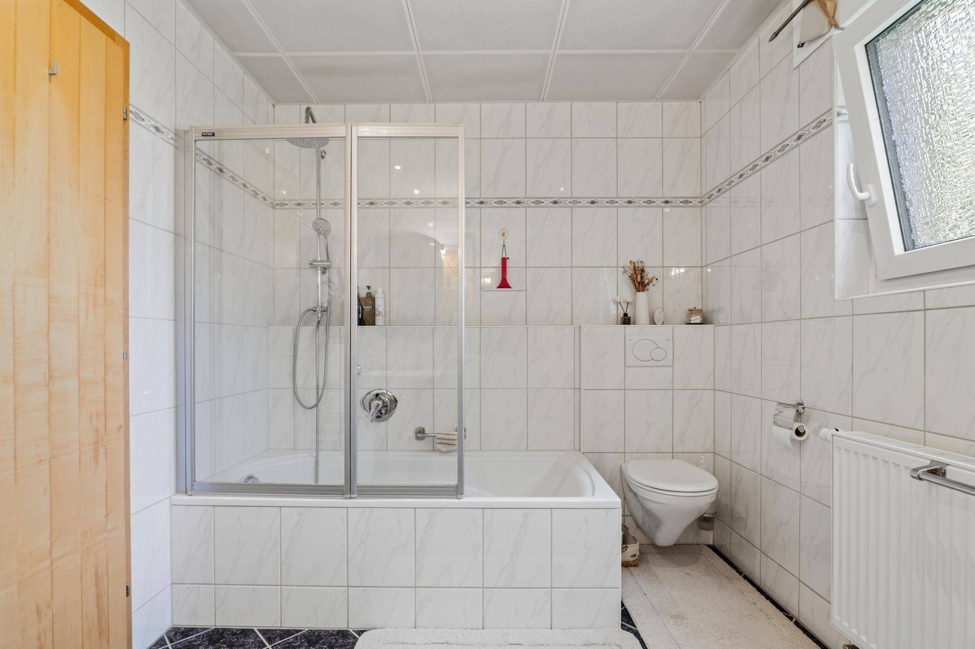 Helles Badezimmer mit Badewanne, Duschabtrennung und Wand-WC.