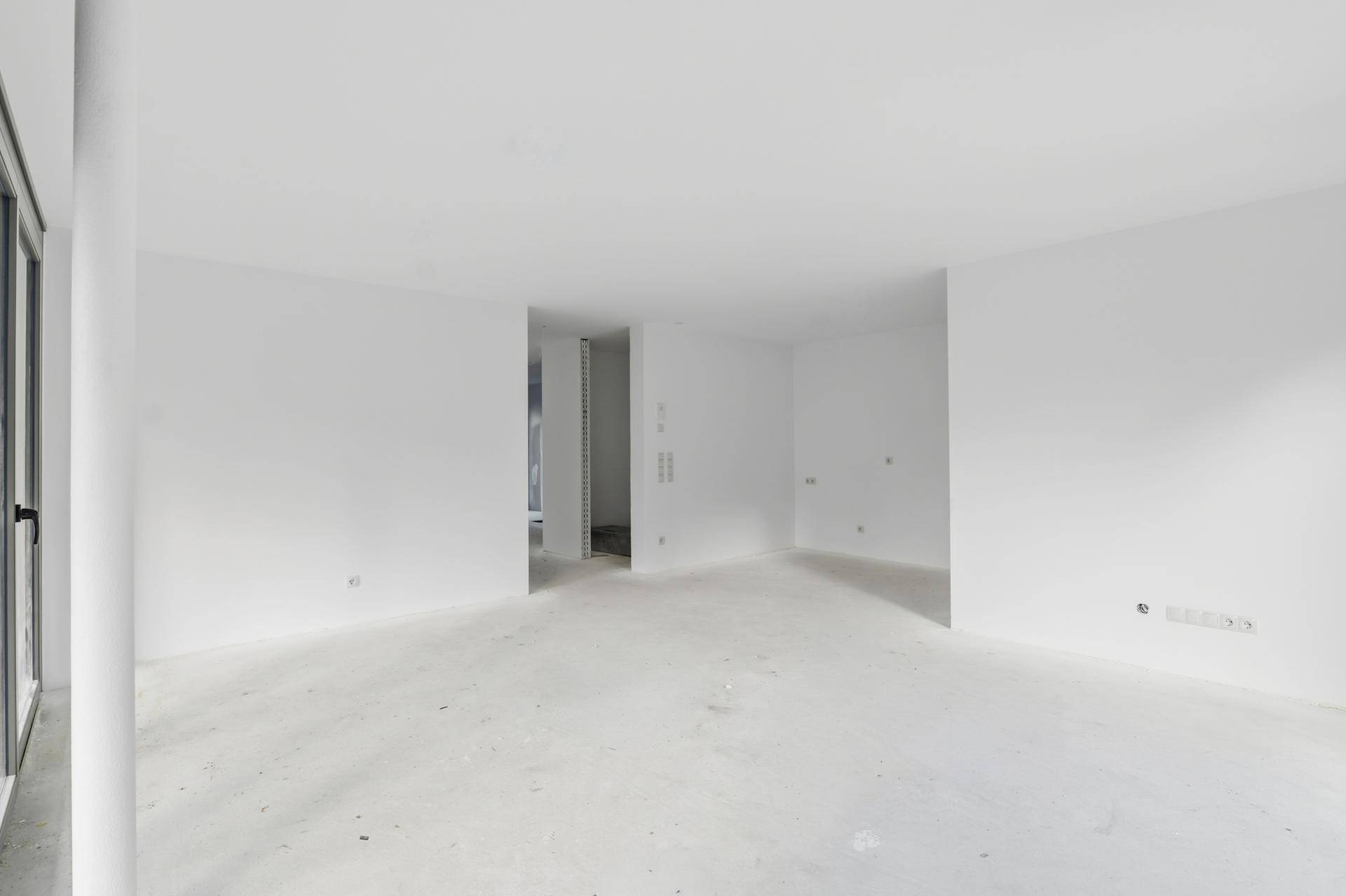 Geräumiger, unmöblierter Wohnbereich mit großen Fenstern und hellem Betonboden, ideal für individuelle Gestaltung.