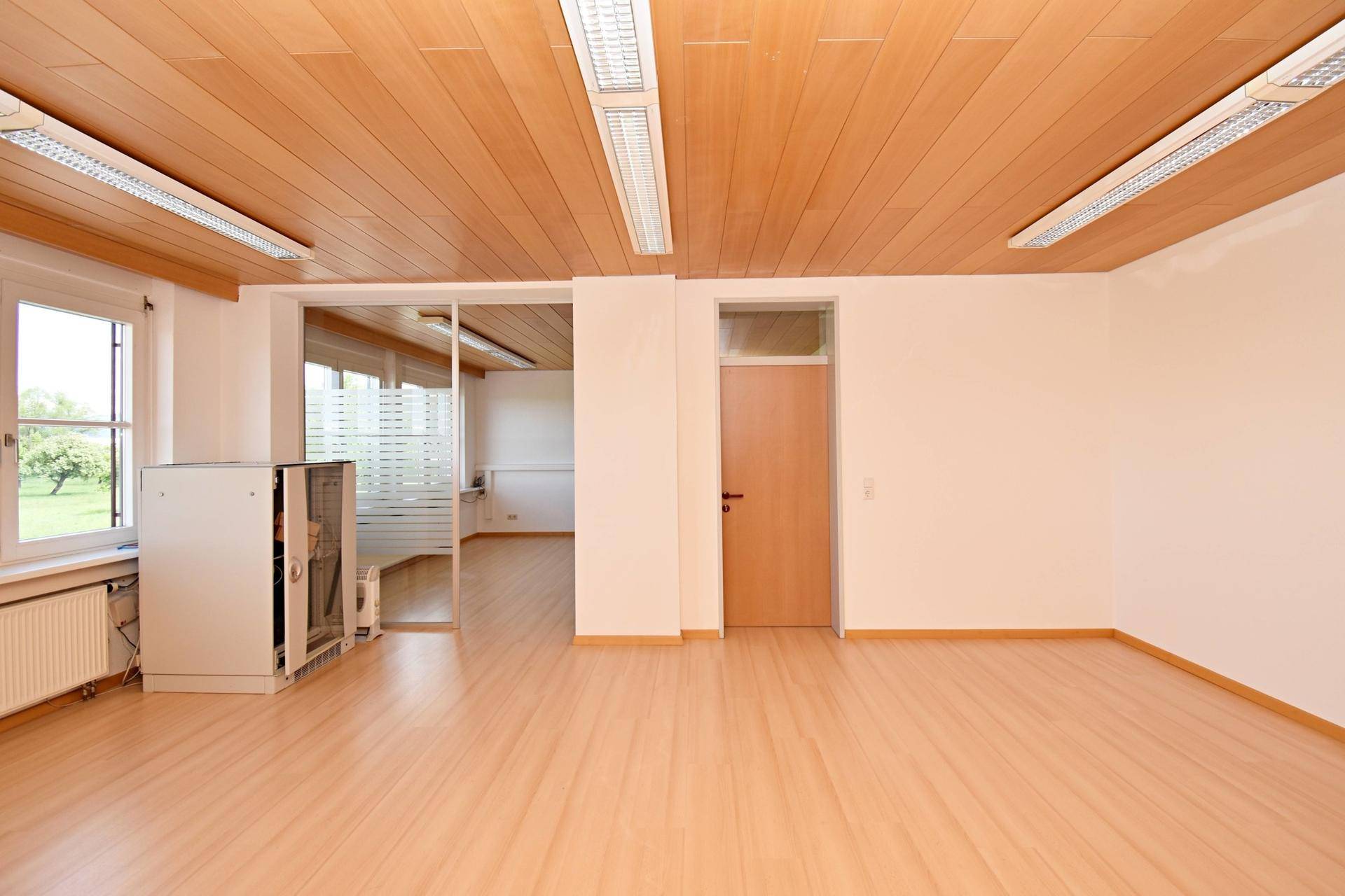 Heller Büroraum mit Laminatboden, Holzdecke und Glastrennwand zu einem weiteren Bereich.