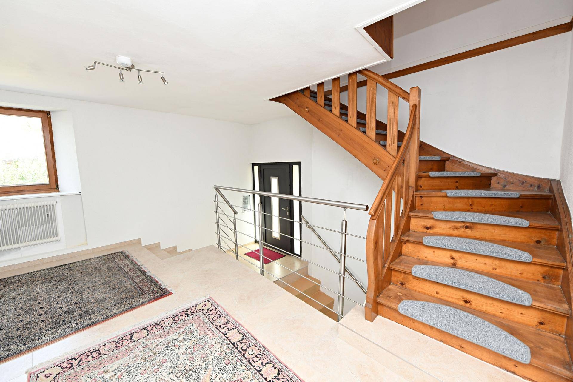 Eingangsbereich mit Holztreppe, modernem Geländer und Fliesenboden.