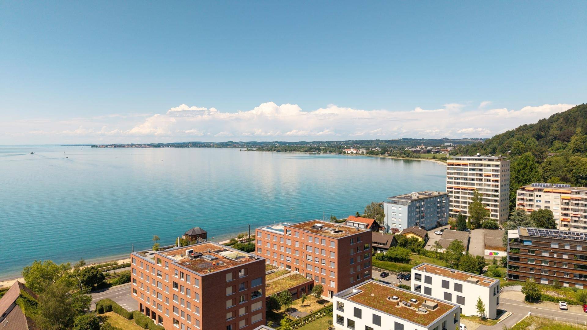 Luftaufnahme der Wohnanlage mit Blick auf den See, die umliegenden Gebäude und die Berge.