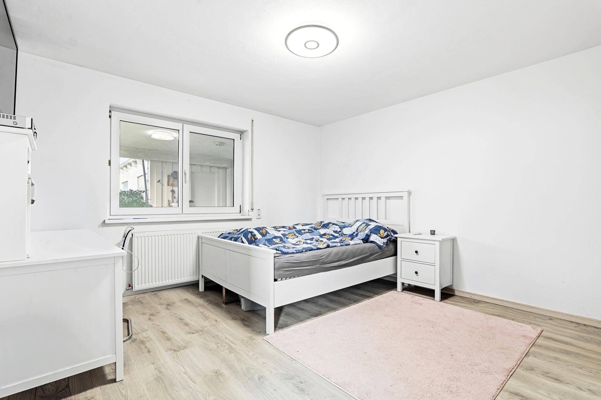 Schlafzimmer mit Laminatboden, weißem Bett und Fenster.
