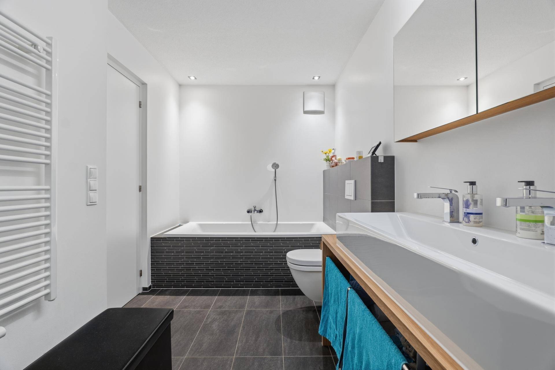 Helles Badezimmer mit Badewanne, modernem Waschbecken und dunklen Bodenfliesen.