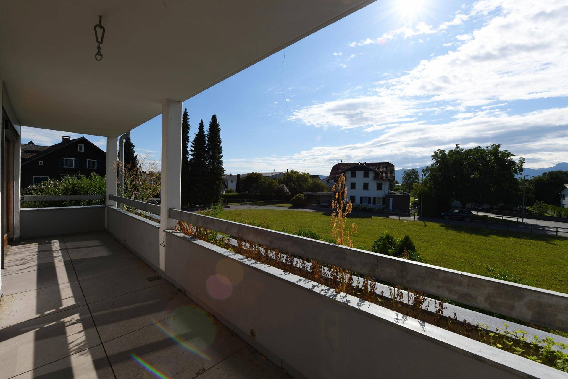 Sonniger Balkon mit weitem Blick über grüne Felder und die umliegende Berglandschaft.