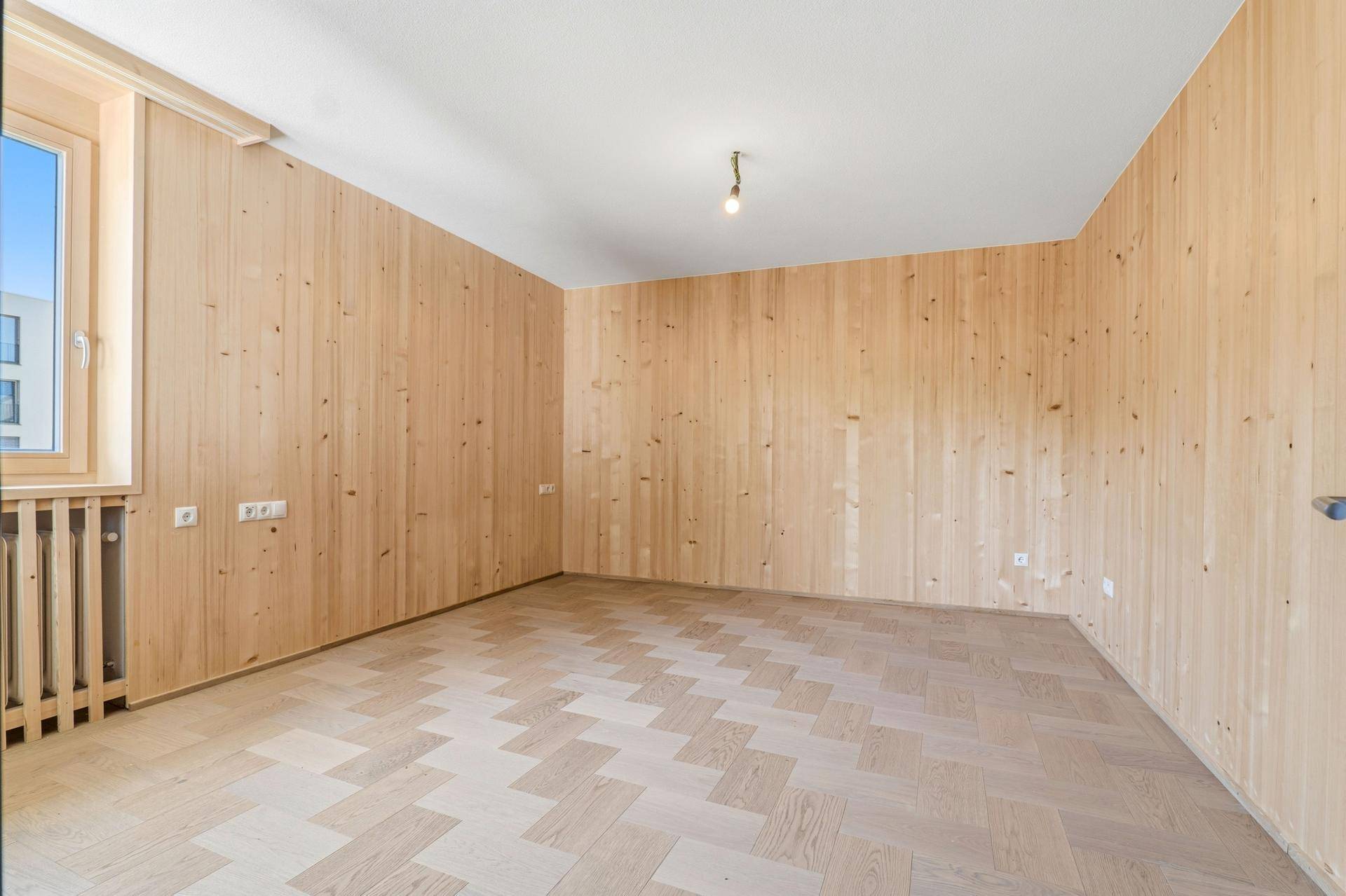 Geräumiger Raum mit Holzwandverkleidung und Fischgrätparkett, bereit zur Einrichtung.