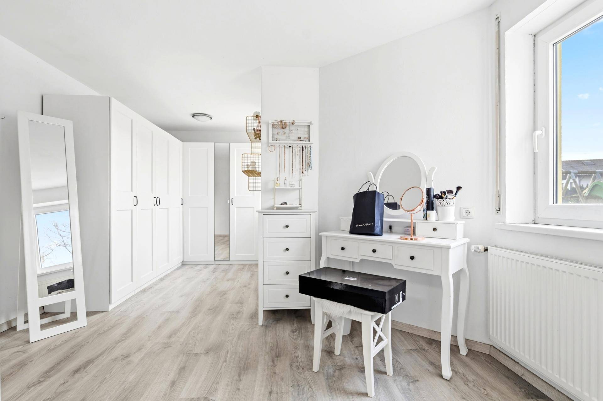 Helles Zimmer mit Laminatboden, weißen Schränken und Schminktisch.