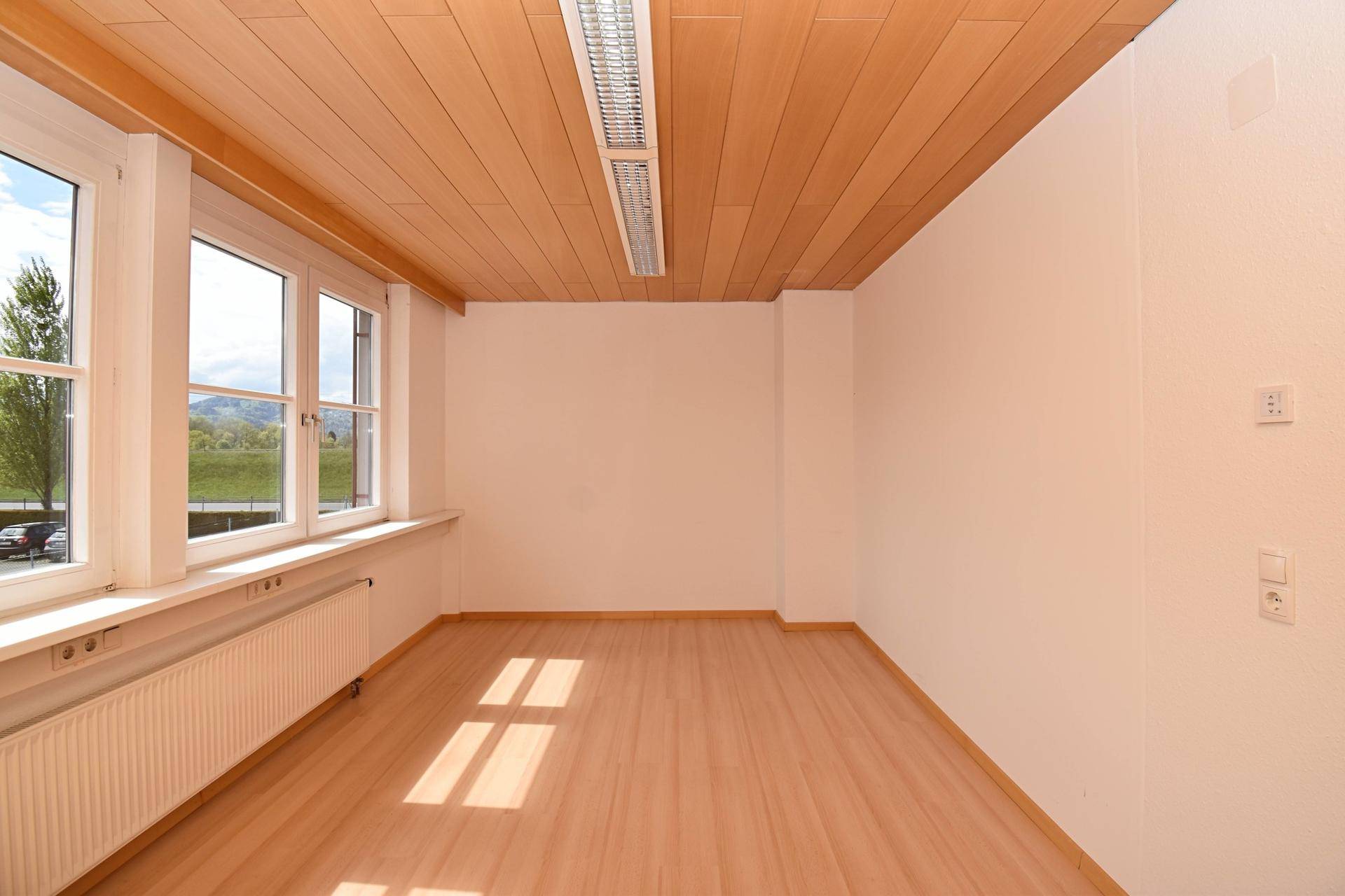 Helles Büro mit Laminatboden, Holzdecke und Fenstern mit Blick auf die Umgebung.