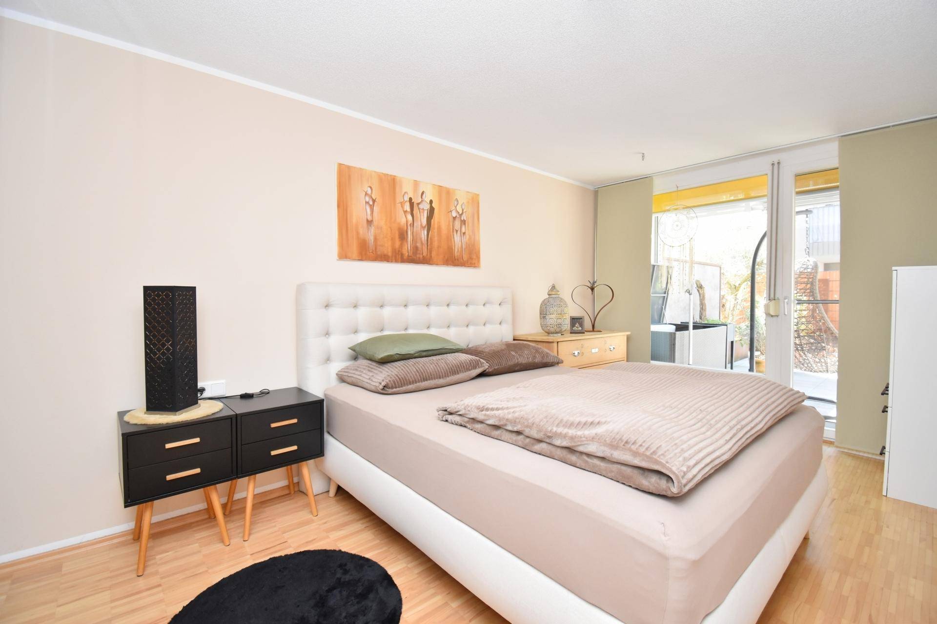 Helles Schlafzimmer mit Doppelbett, Nachttischen und Zugang zu einem Balkon oder einer Terrasse.